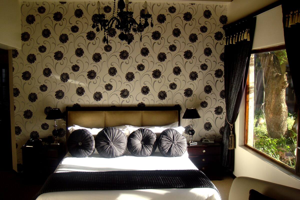 A bedroom with a large bed, a chandelier, and a view of greenery through a window.