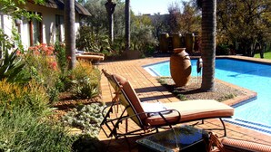 A pool area with lounge chairs and a large decorative urn. - Lourie Lodge (Sandton)