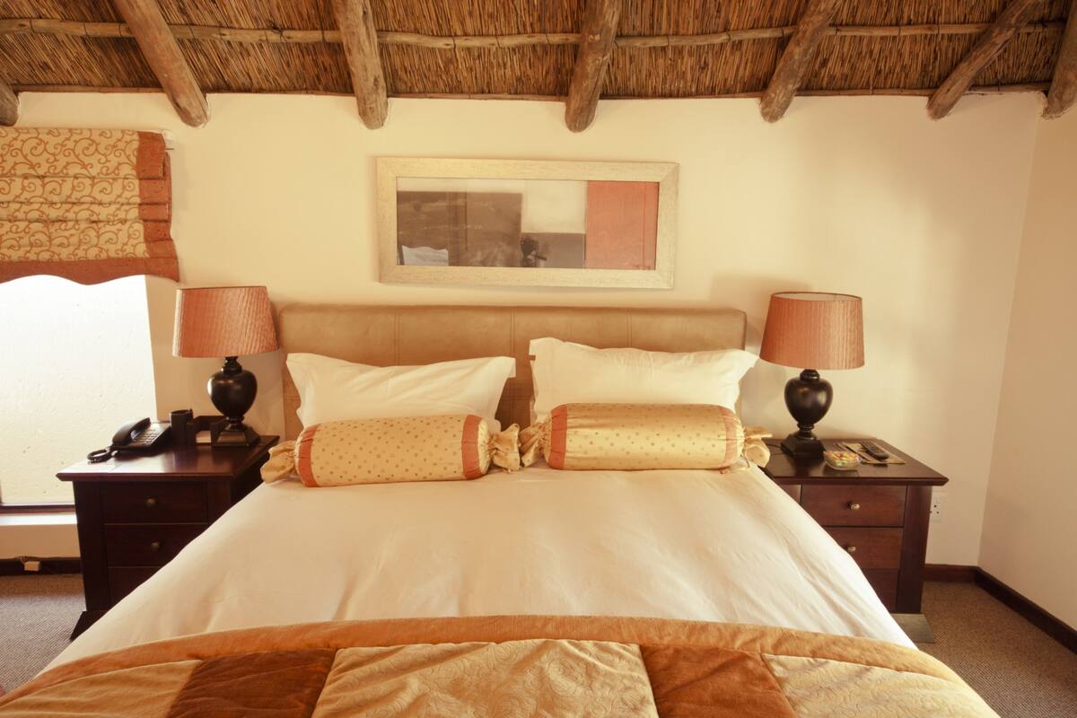 A hotel room with a bed, two bedside tables, a nightstand, a mirror, and a window with curtains.