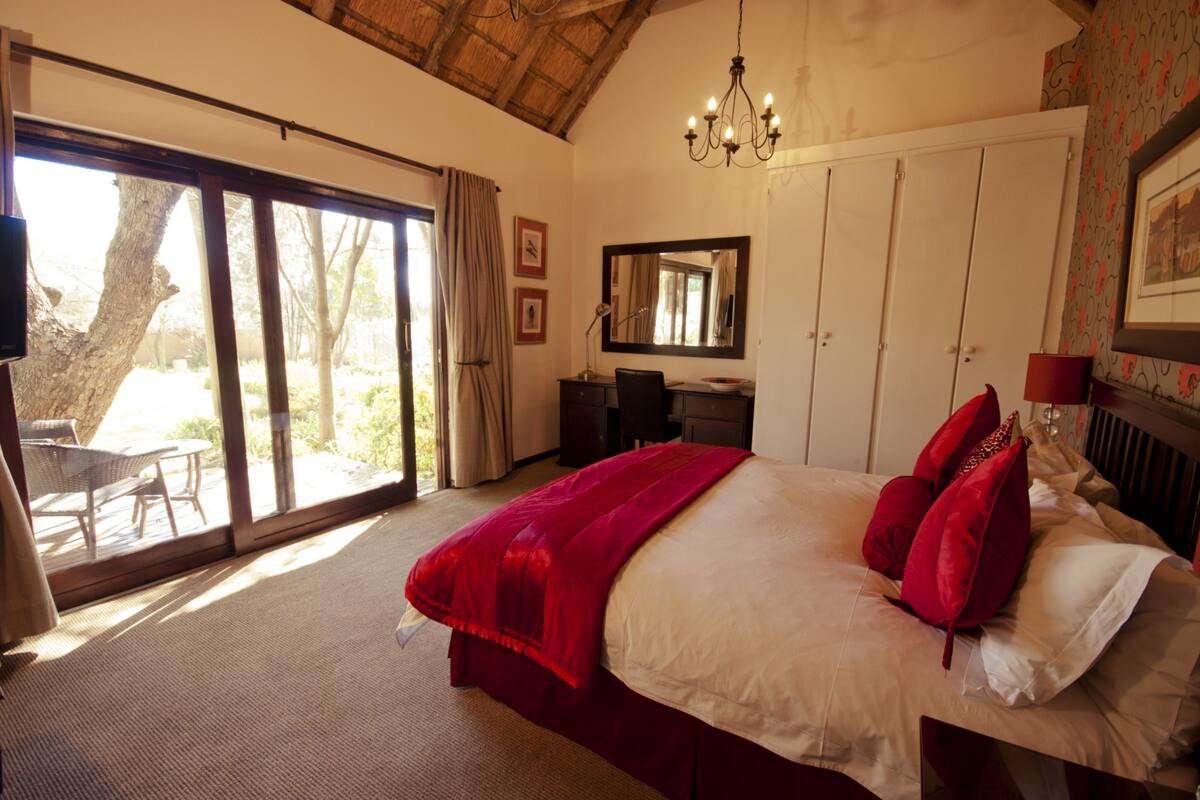 A bedroom with a large bed, a desk, a chair, and a view of the outdoors through a sliding door.