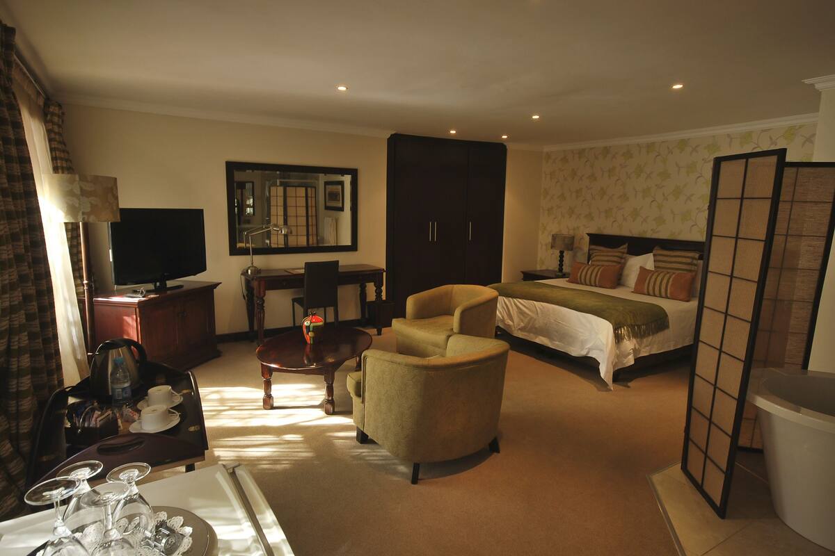 A hotel room with a bed, a sofa, a desk with a TV, a mirror, and a view of the outside.