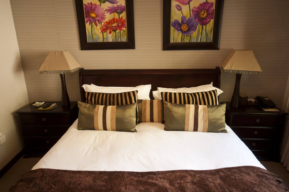 A neatly made bed with striped pillows, a brown blanket, and two bedside tables with lamps.