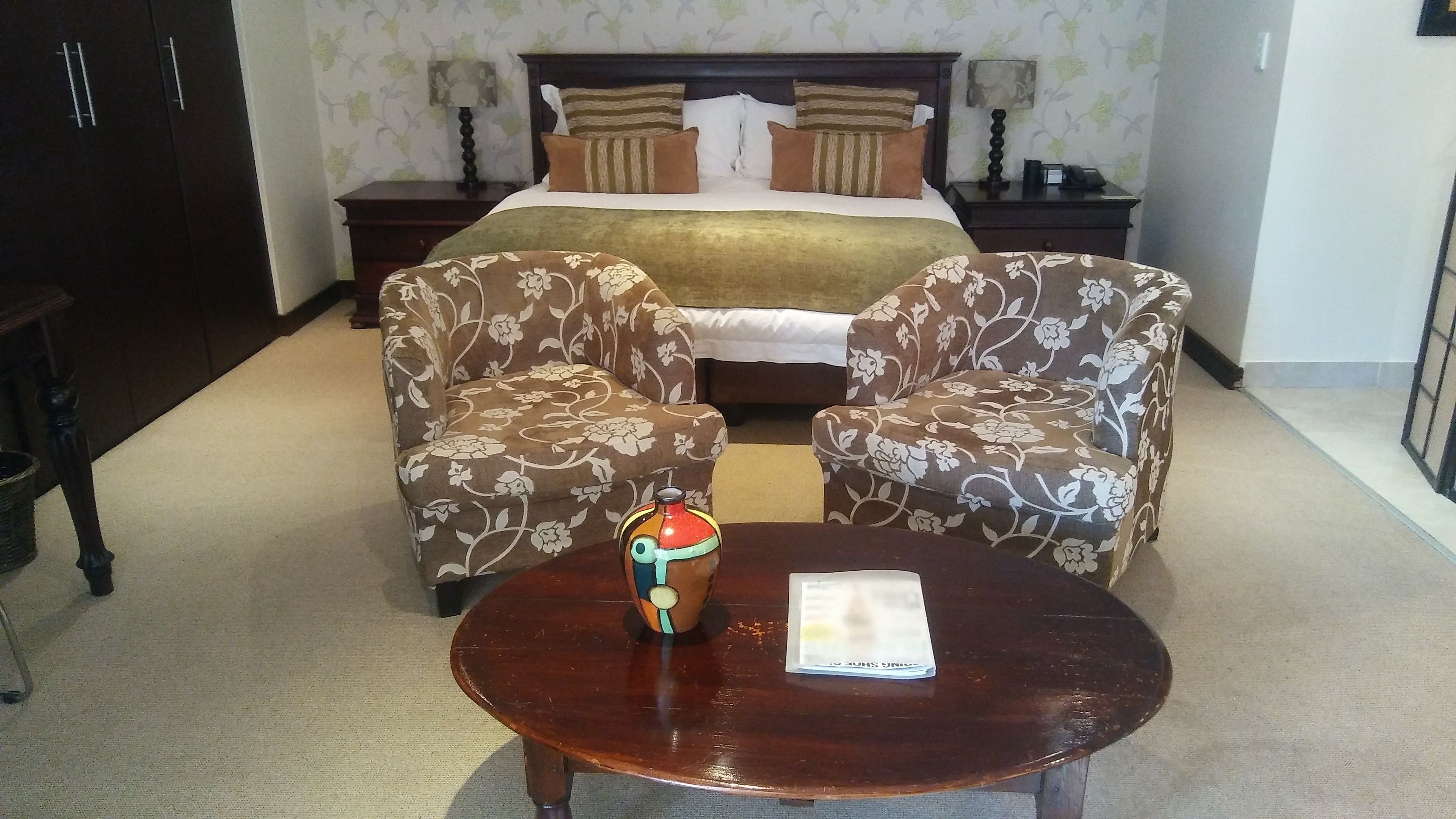 Une chambre d’hôtel avec un lit, deux fauteuils, une petite table et un vase.