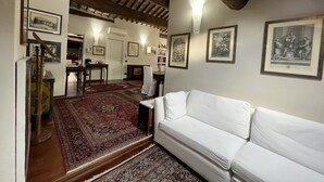 Een kamer met een witte bank, een rood tapijt met patroon en lijstwerken aan de muren.