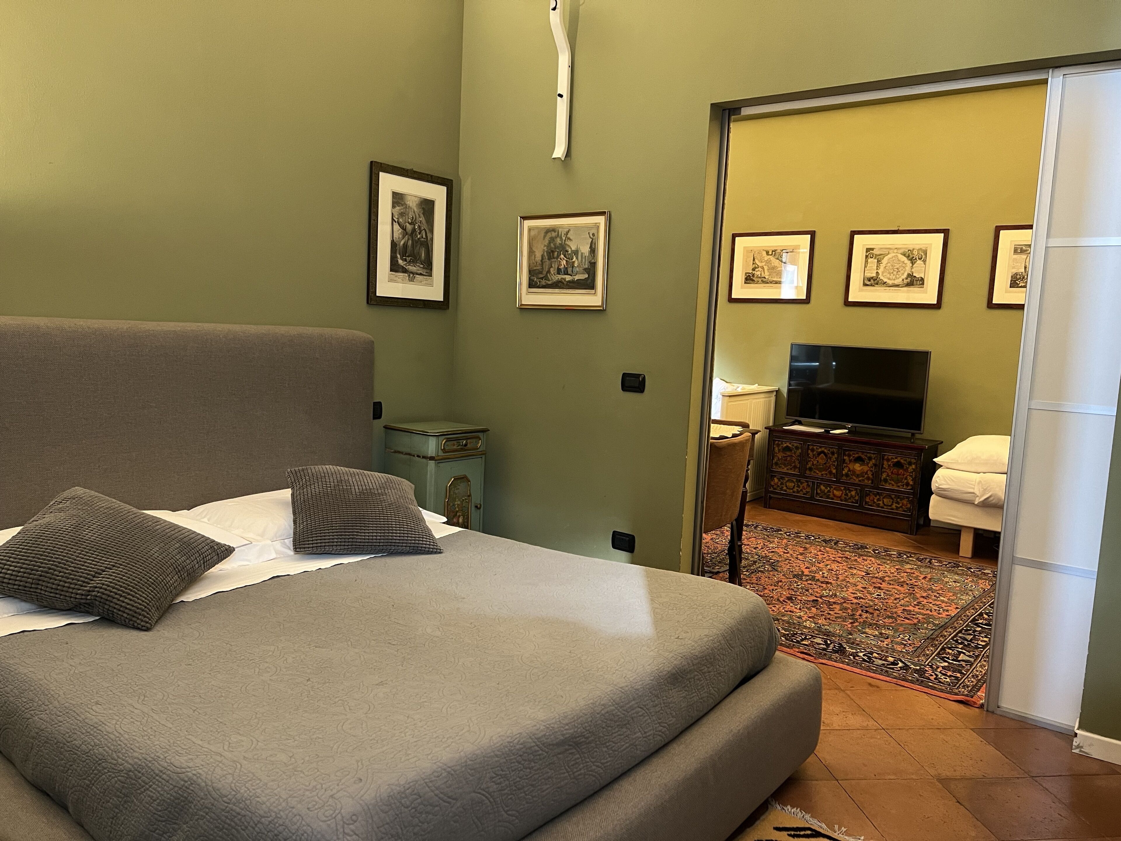 A bedroom with a bed, pillows, a dresser, a television, and framed pictures on the wall.