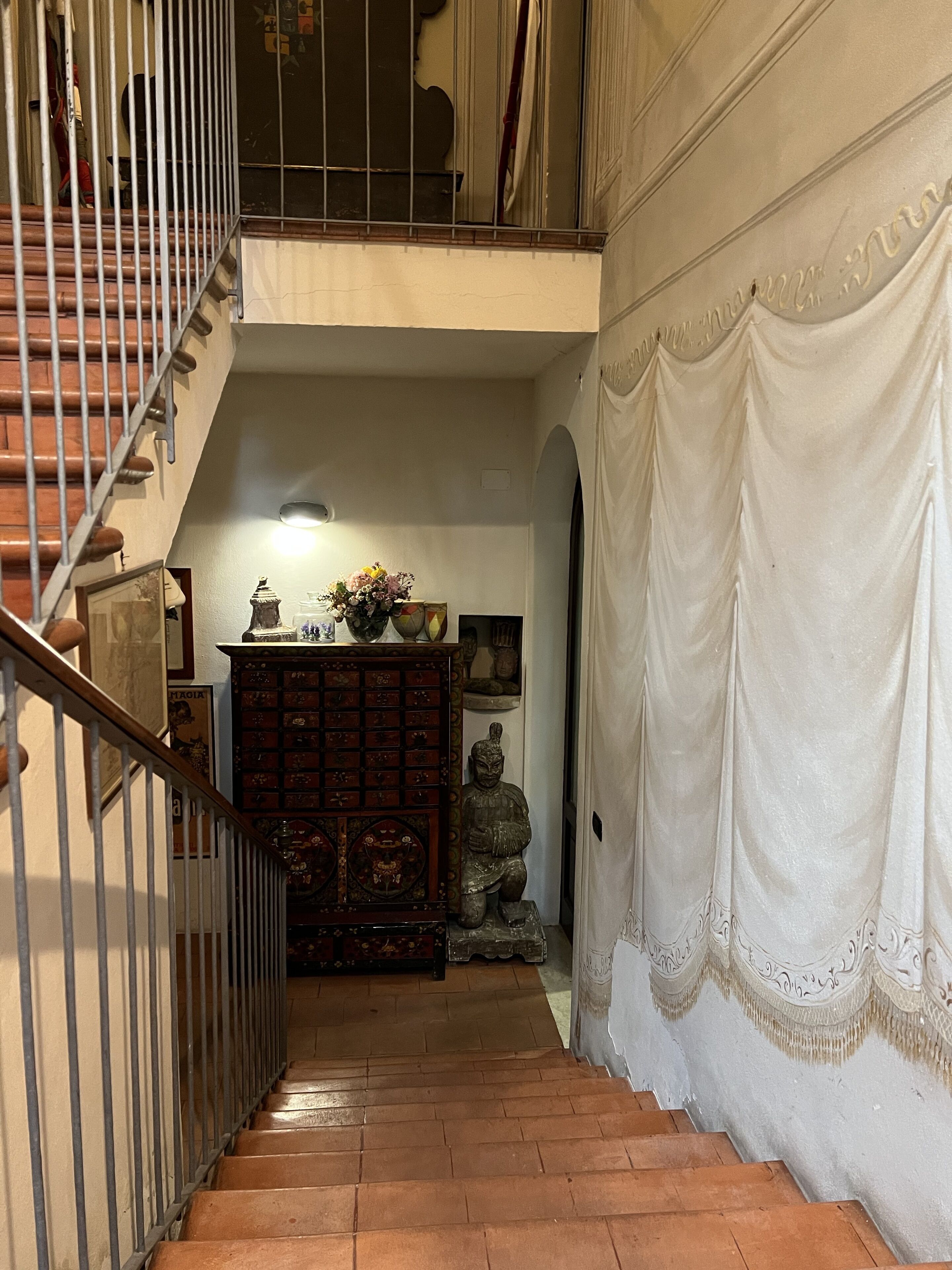 A staircase with a wooden handrail leading to a landing. There is a decorative cabinet with various items on it, and a statue on the landing.