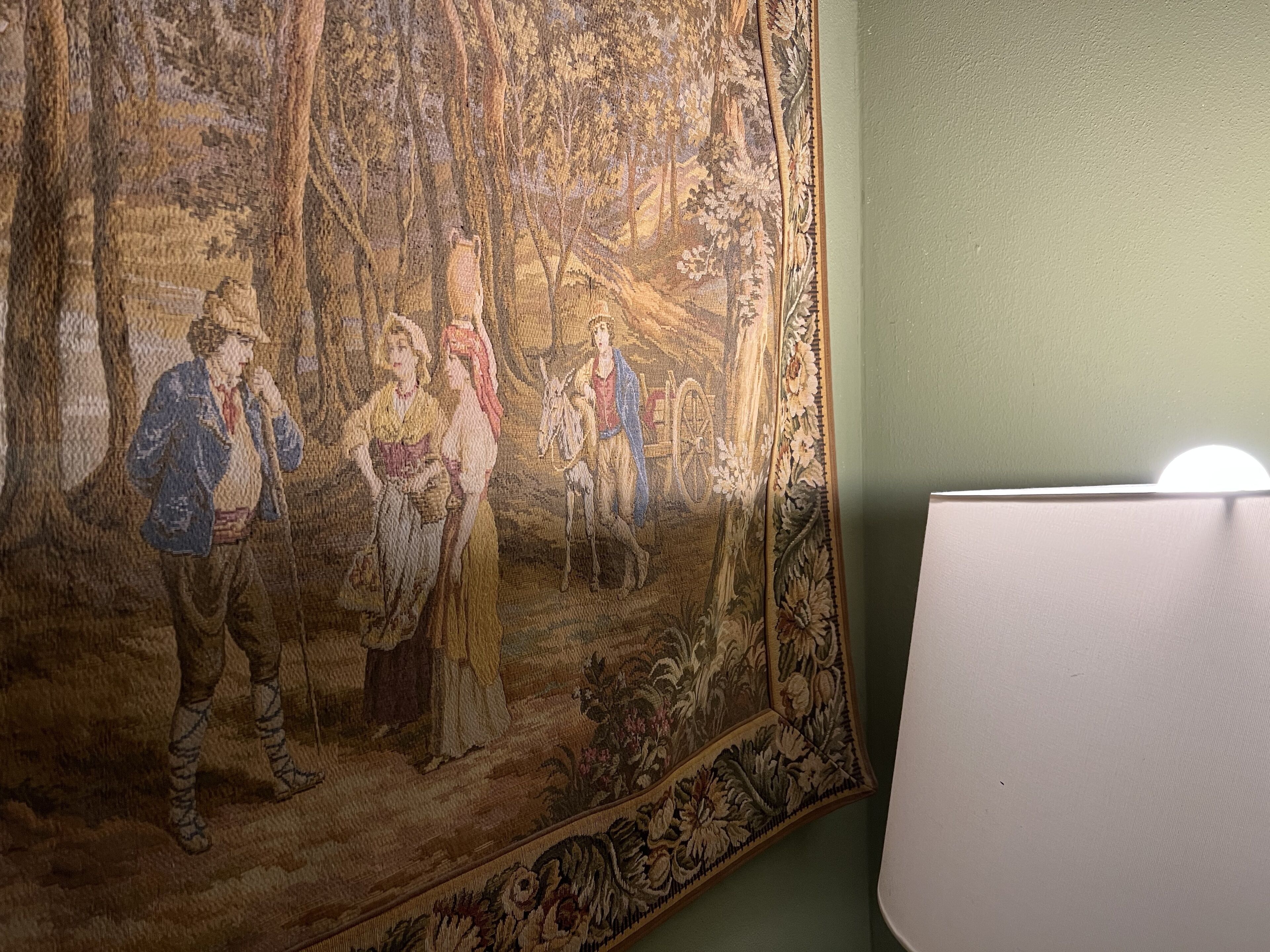 Une tapisserie représentant une scène de forêt, un cheval et des personnages vêtus de costumes d’époque.