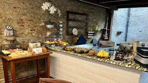 Een sfeervol café met een houten toonbank vol gebak en belegde broodjes, een stenen muur en een kleine tafel met een stoel.