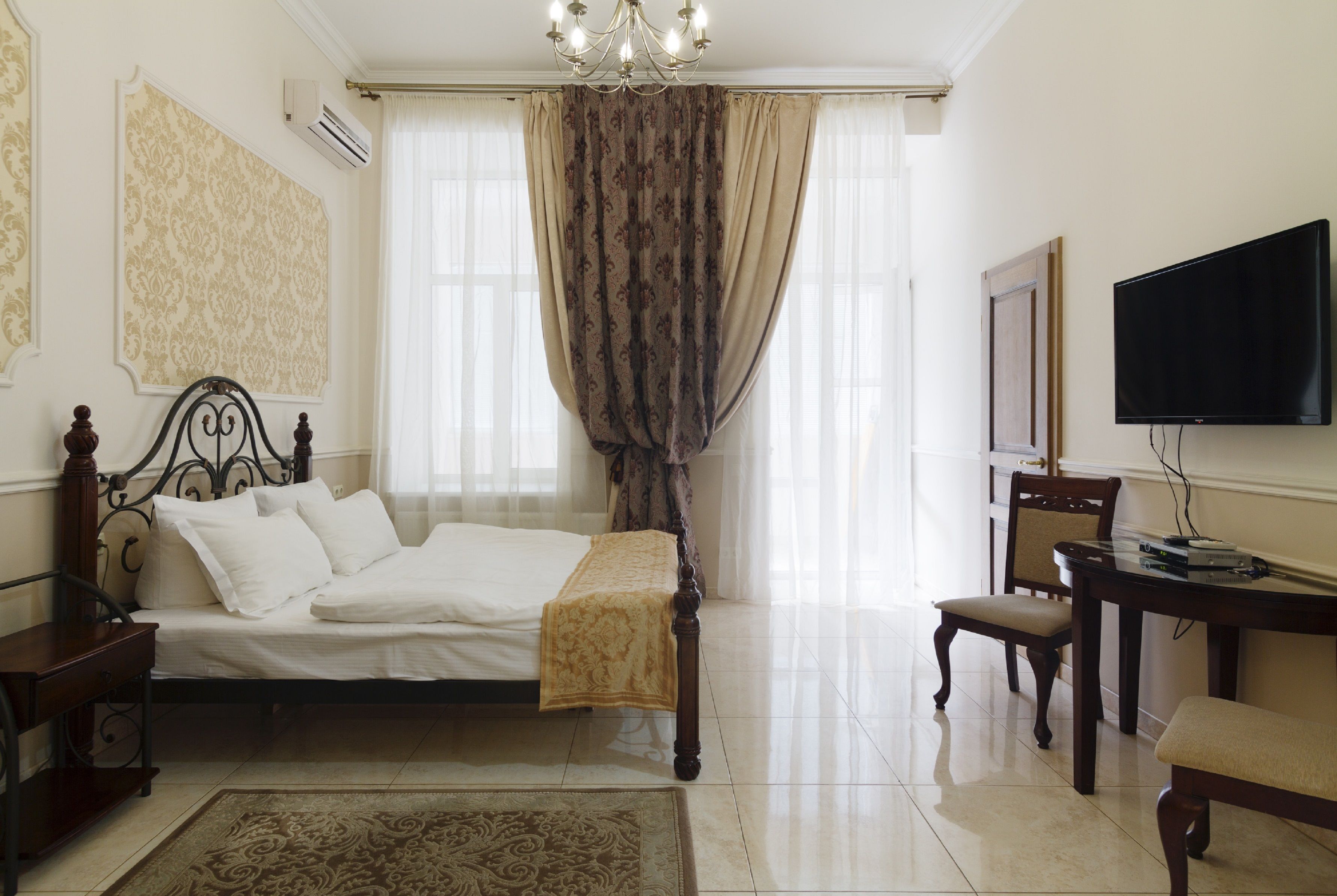 A bedroom with a bed, bedside table, chair, TV, and curtains.