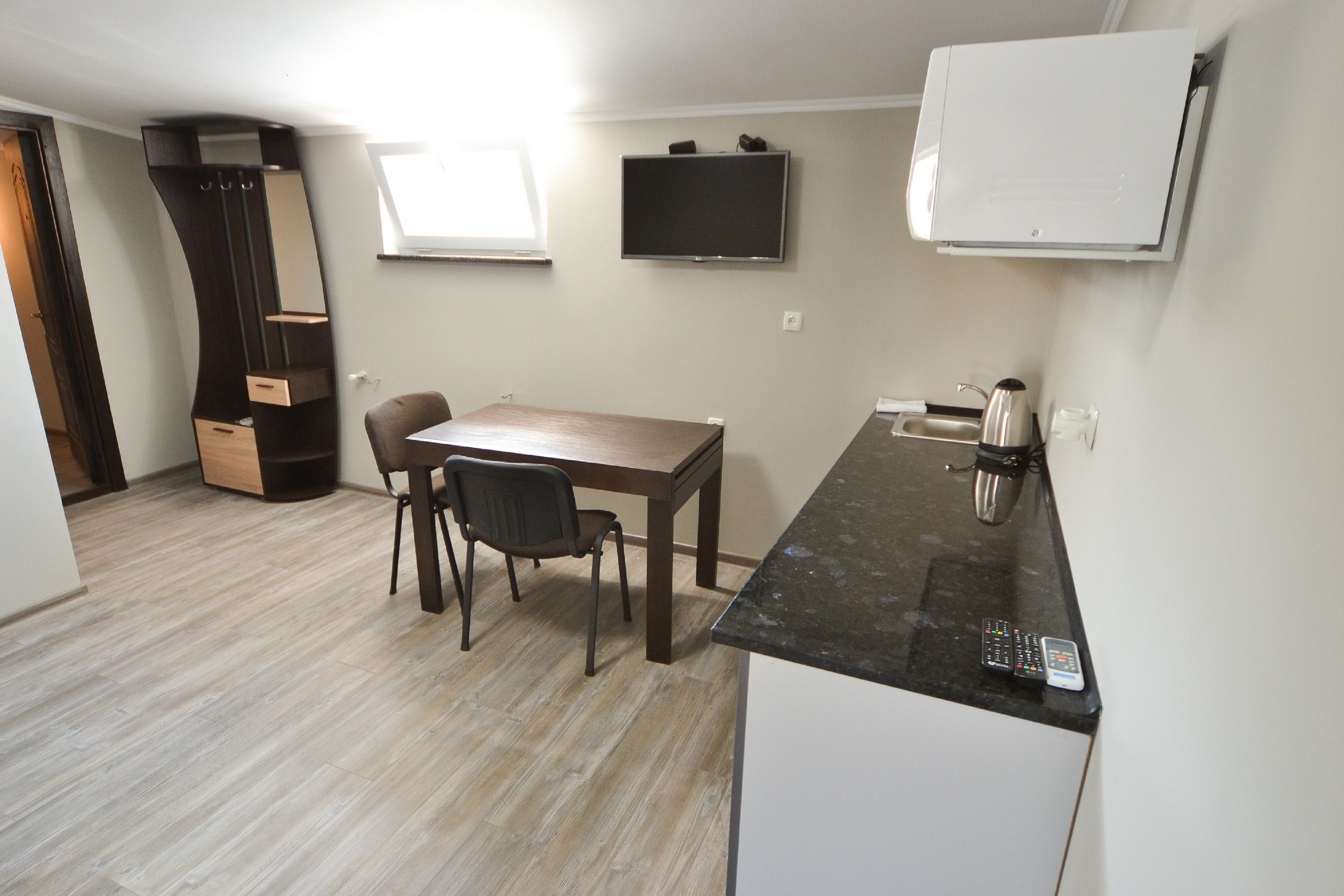 A compact kitchen with a dining table and chairs, a built-in oven, and a flat-screen TV mounted on the wall.