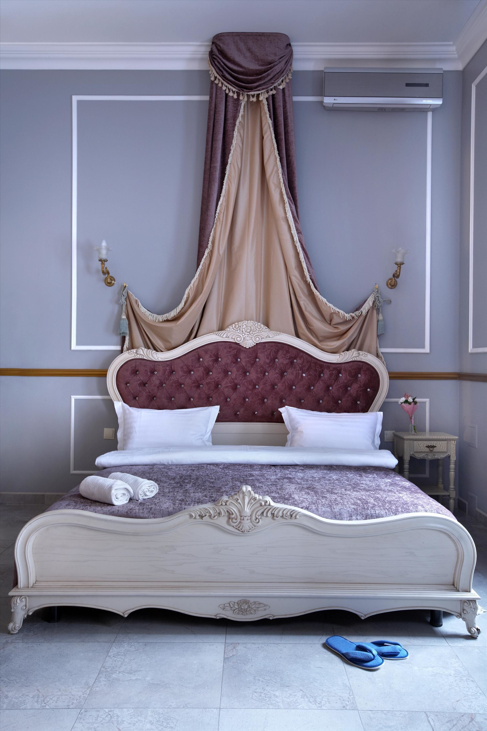 A bed with a canopy, white bedding, and a pair of slippers on the floor.