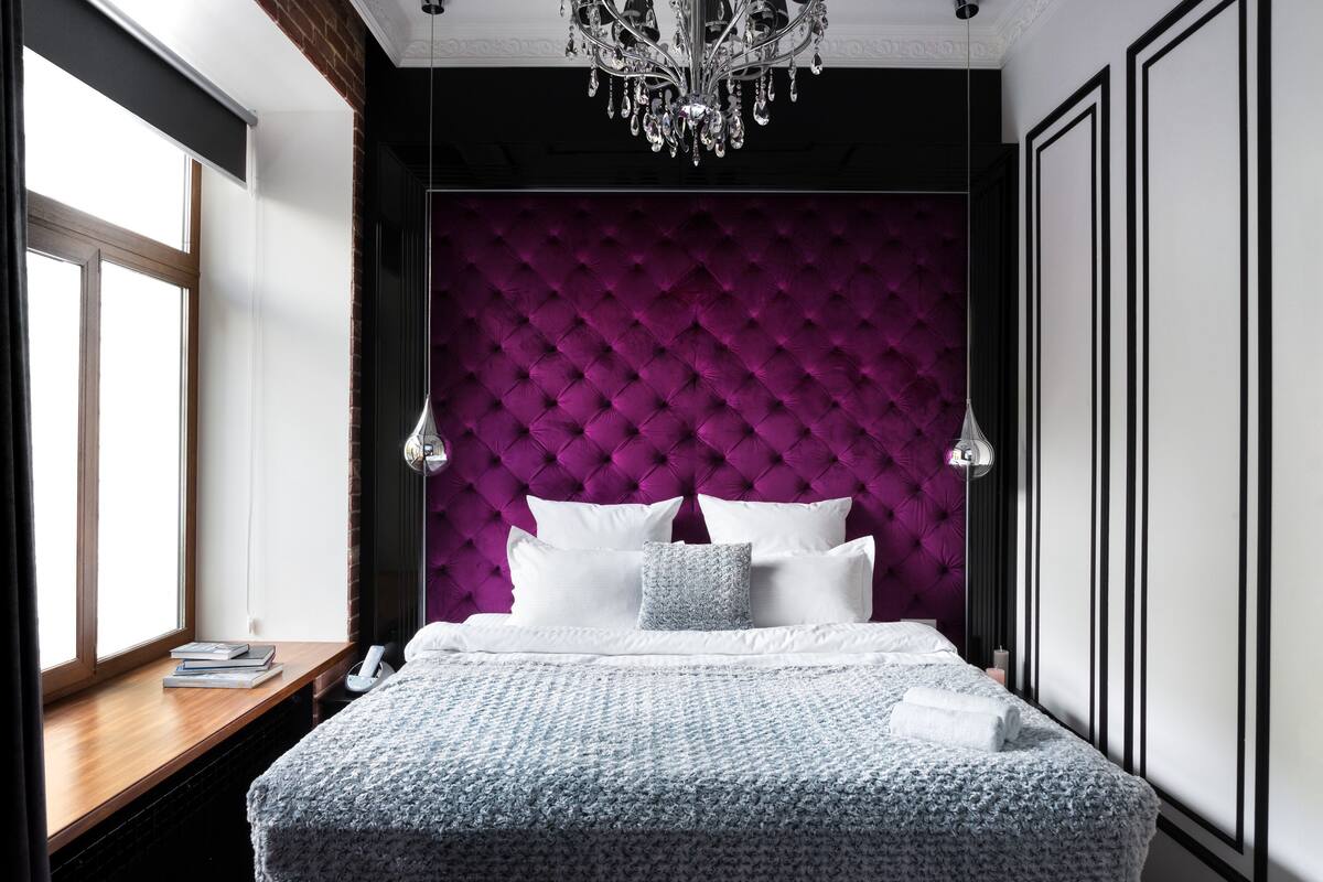 Un dormitorio con cabecera capitonada, mesita de noche de madera y candelabro.