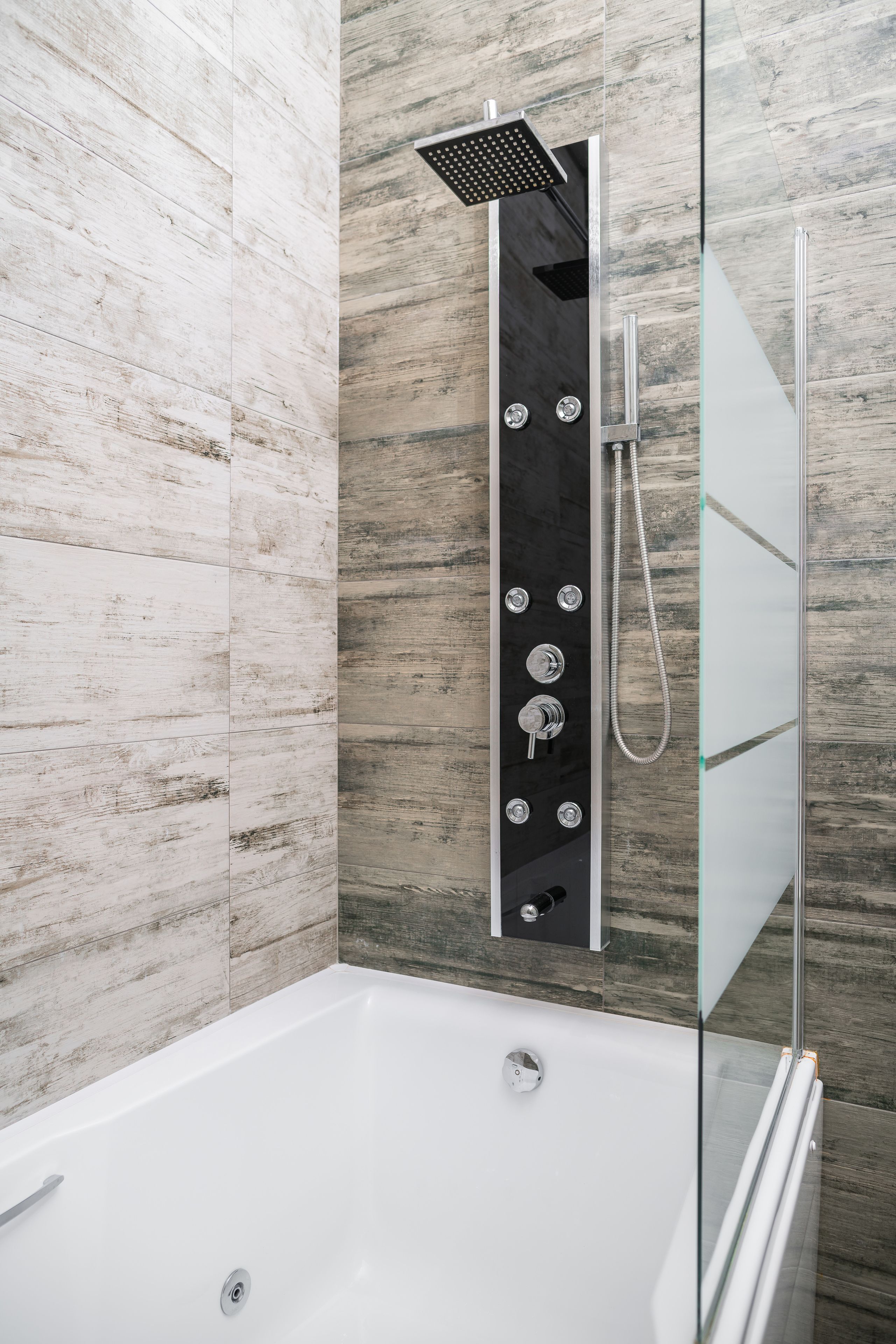 A modern bathroom with a glass-enclosed shower, a white bathtub, and a wooden-textured wall.