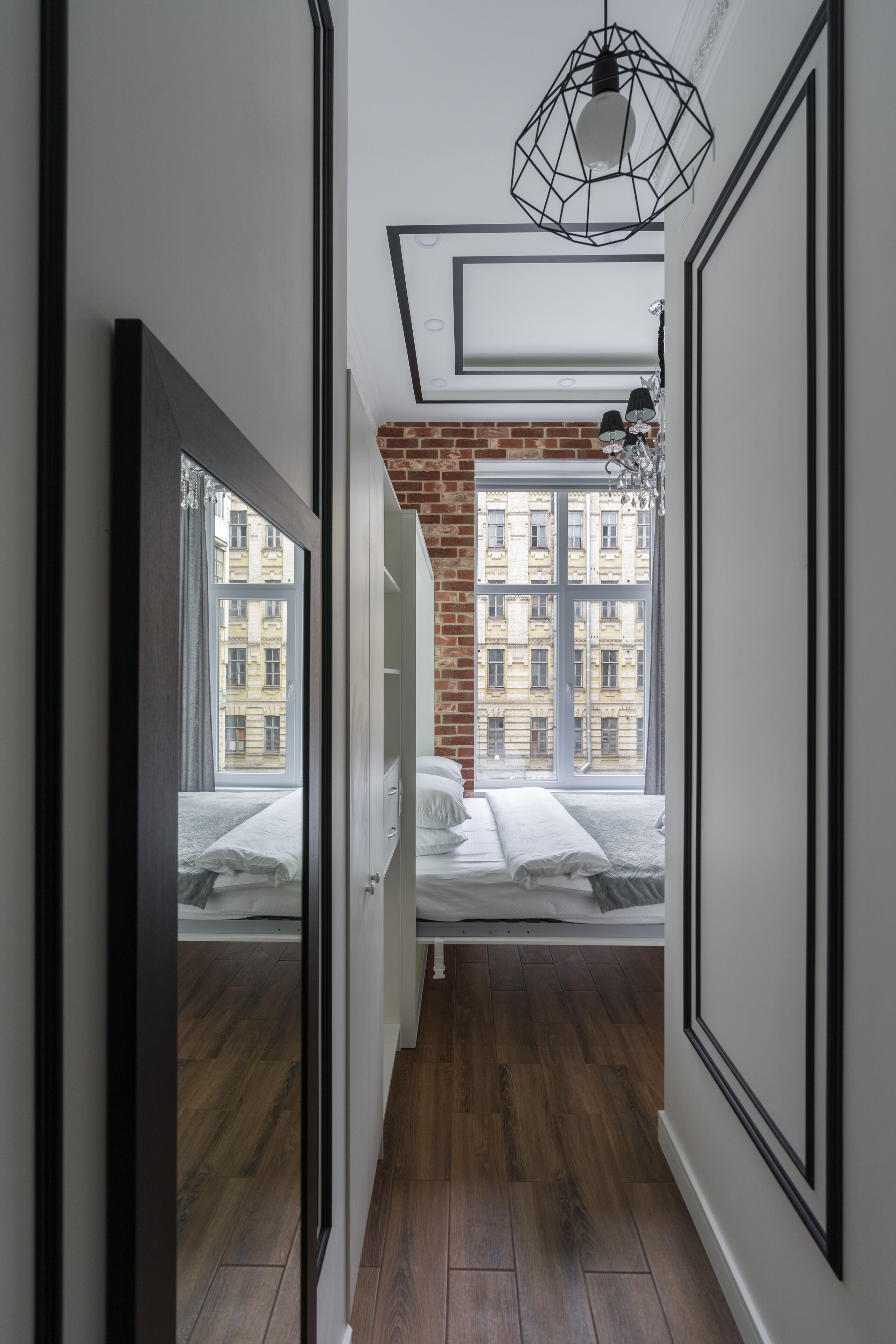 Un pasillo estrecho con suelo de madera, una cama con ropa de cama blanca y una pared de ladrillo.