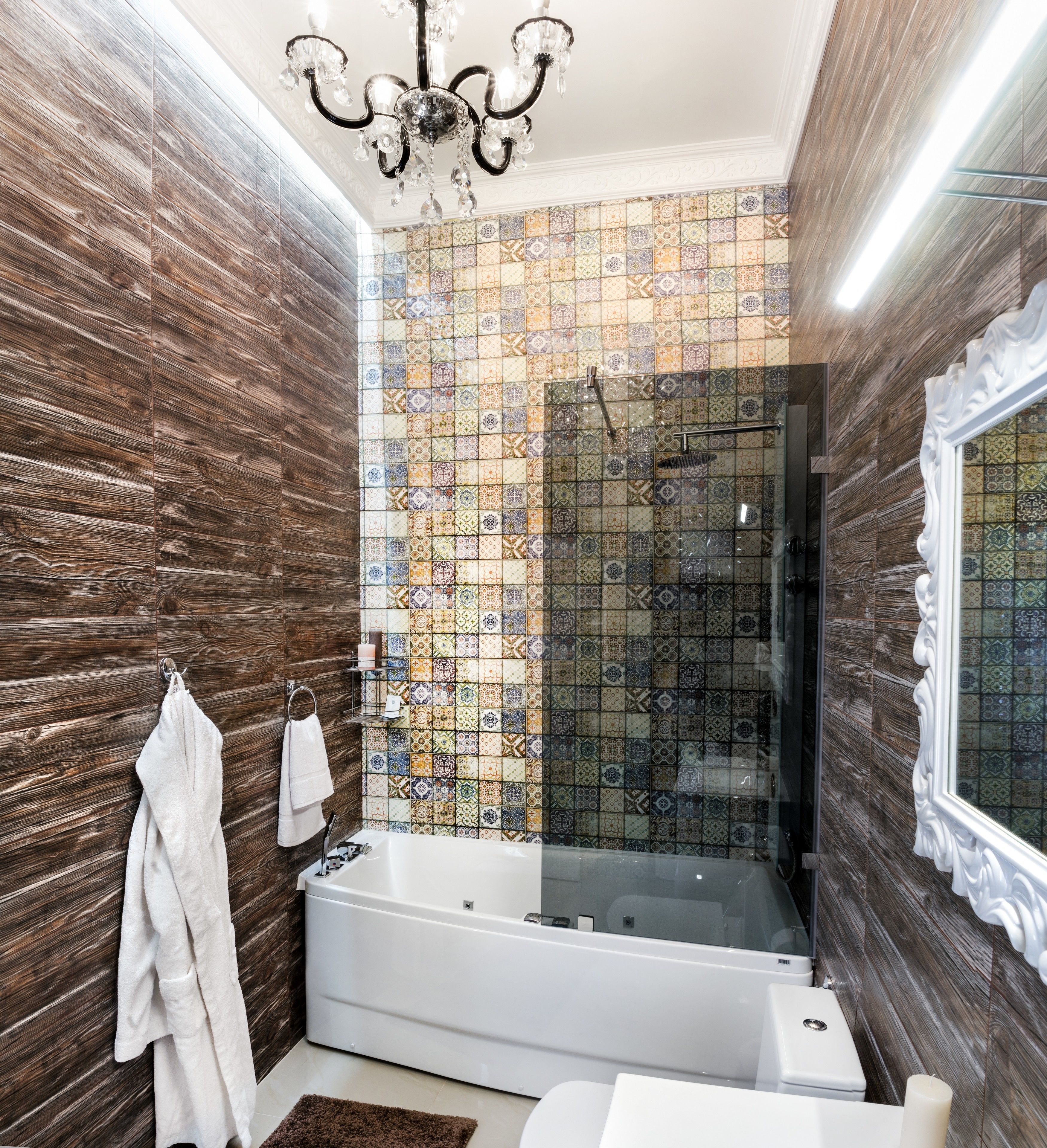 A modern bathroom with a wooden wall, a tiled shower wall, a white bathtub, and a white sink.