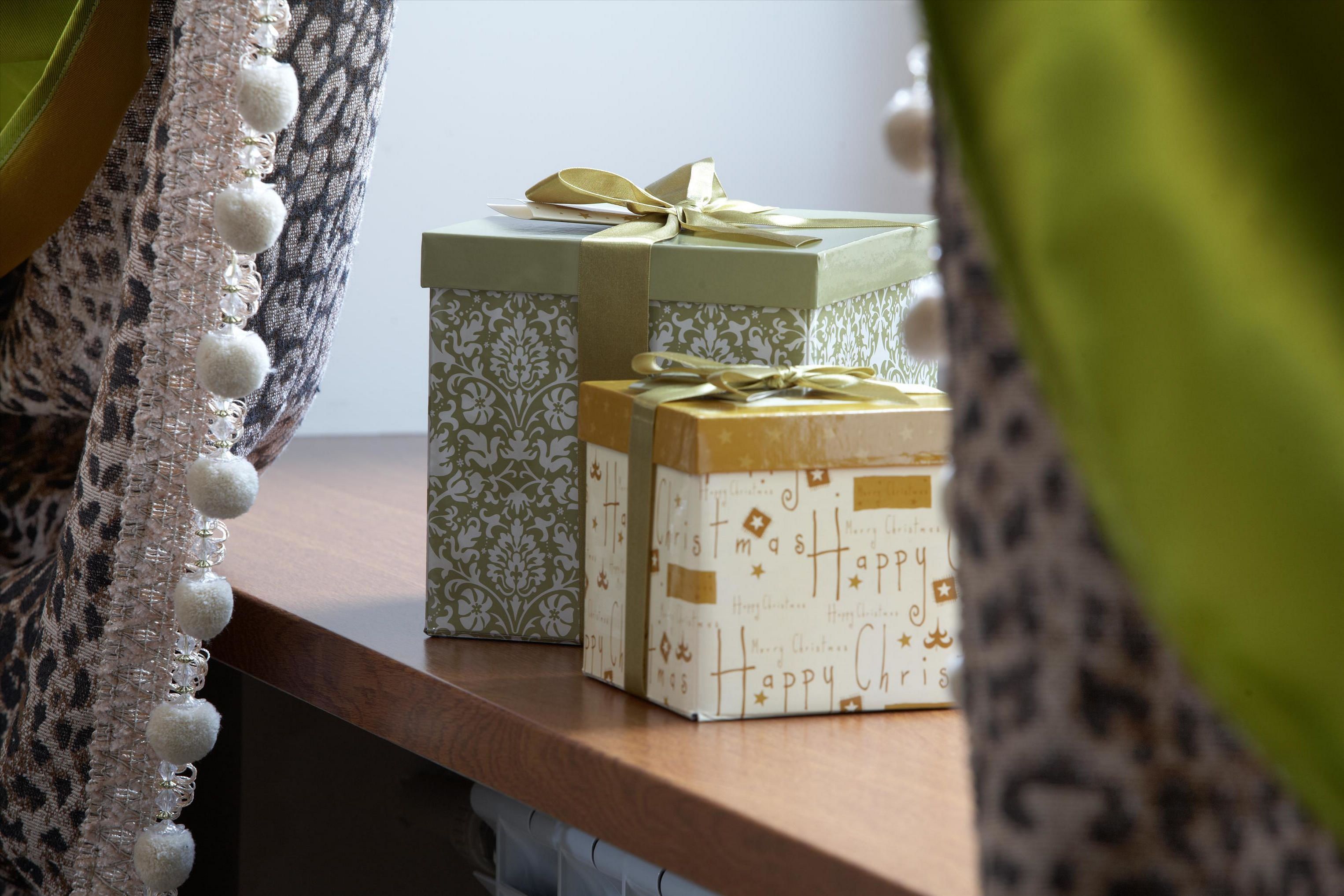 Deux boîtes à cadeaux sont posées sur une surface en bois : l’une est ornée d’un motif vert et blanc, l’autre d’un motif doré et blanc, et les deux sont attachées avec des rubans.