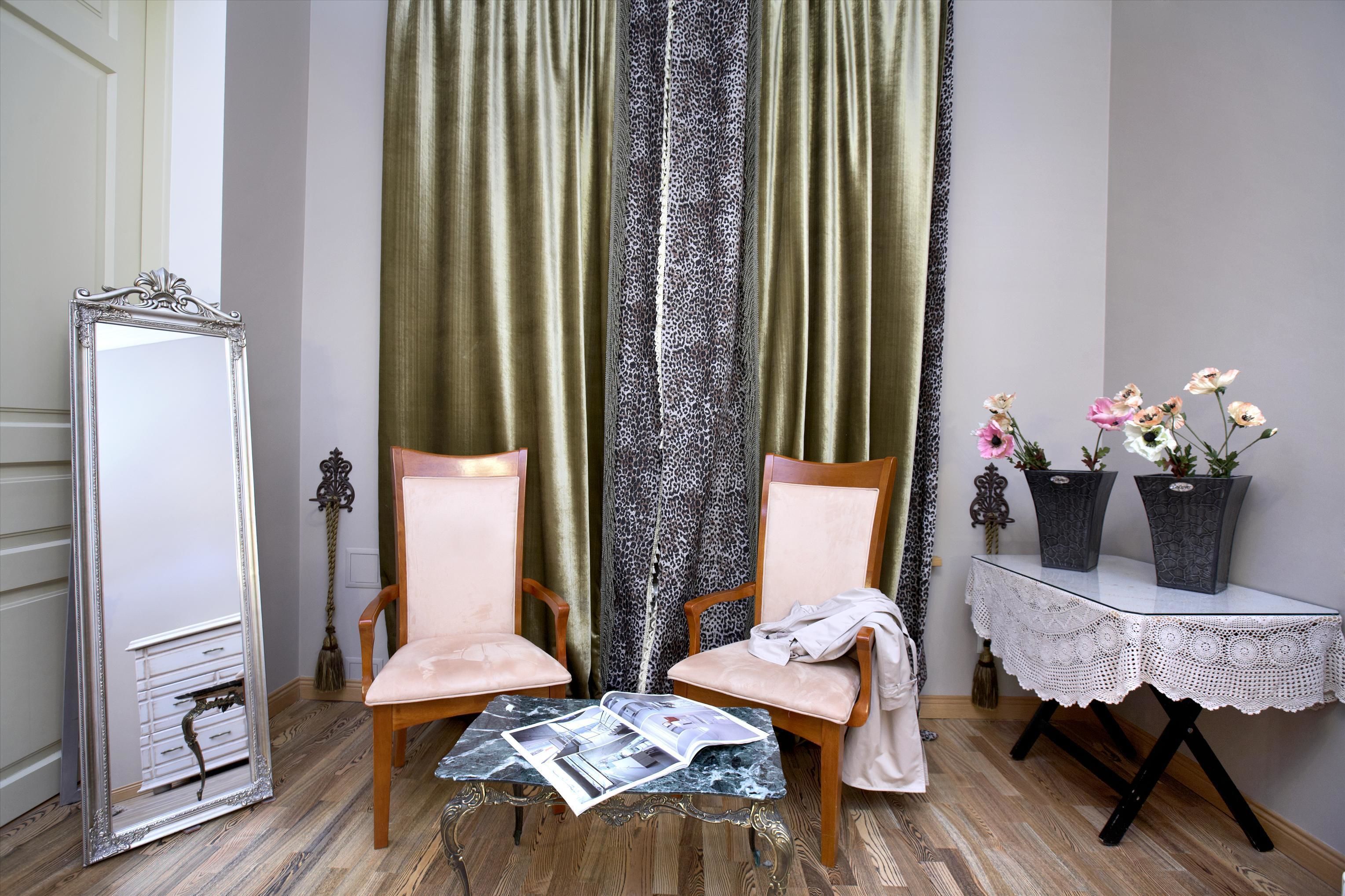 Una habitación con dos sillas de madera, una mesa con revistas, un espejo, un mantel de encaje y dos jarrones de flores.