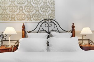 Een netjes opgemaakt bed met witte lakens, twee nachtkastjes met lampen, en een decoratieve muur met een damasten patroon.