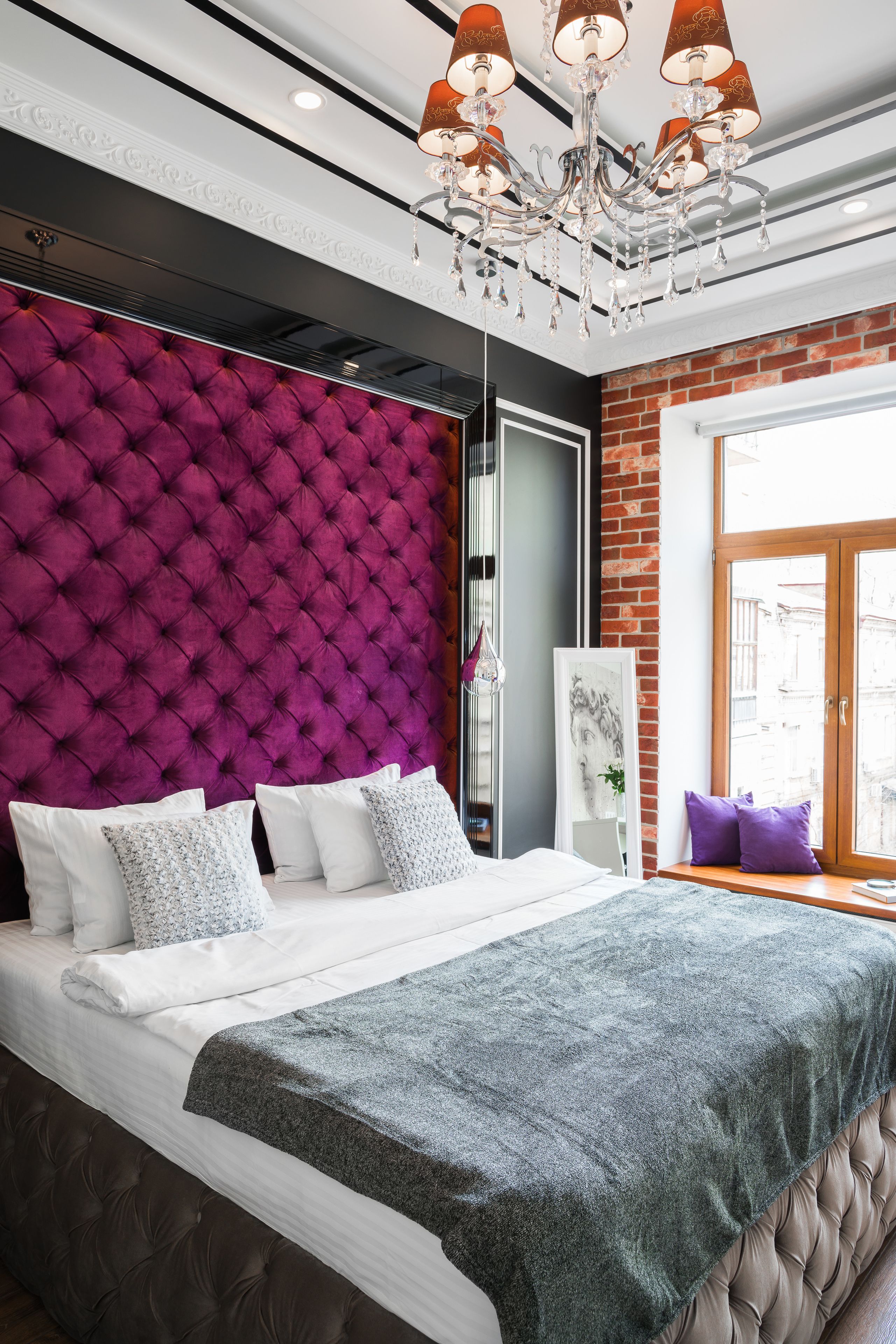Un dormitorio moderno con un cabecero capitonado, una cama grande con ropa de cama blanca, una manta gris y una araña.
