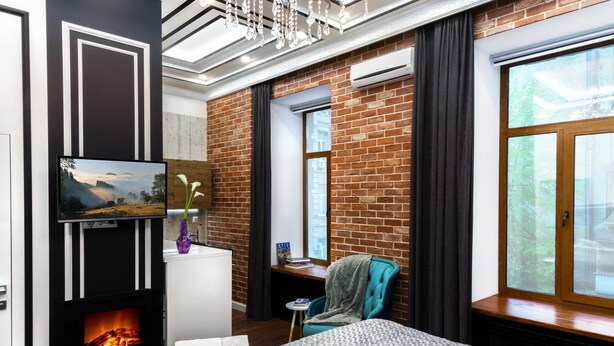 Une chambre d’hôtel moderne dotée d’une cheminée, d’une grande fenêtre offrant une belle vue, d’un fauteuil confortable et d’un lit parfaitement fait.