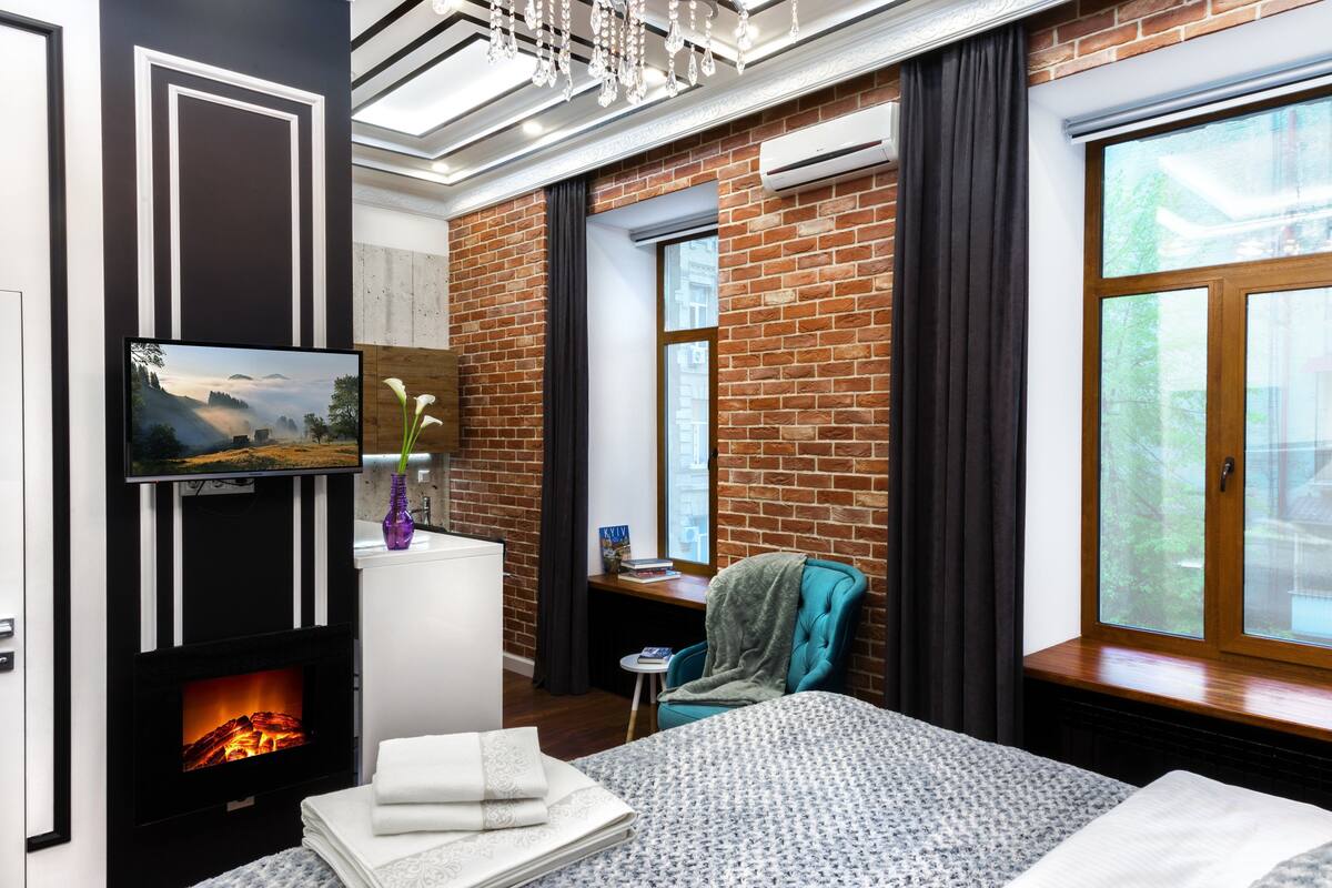 Una habitación de hotel moderna con chimenea, un amplio ventanal con vistas, un sillón cómodo y una cama bien hecha.