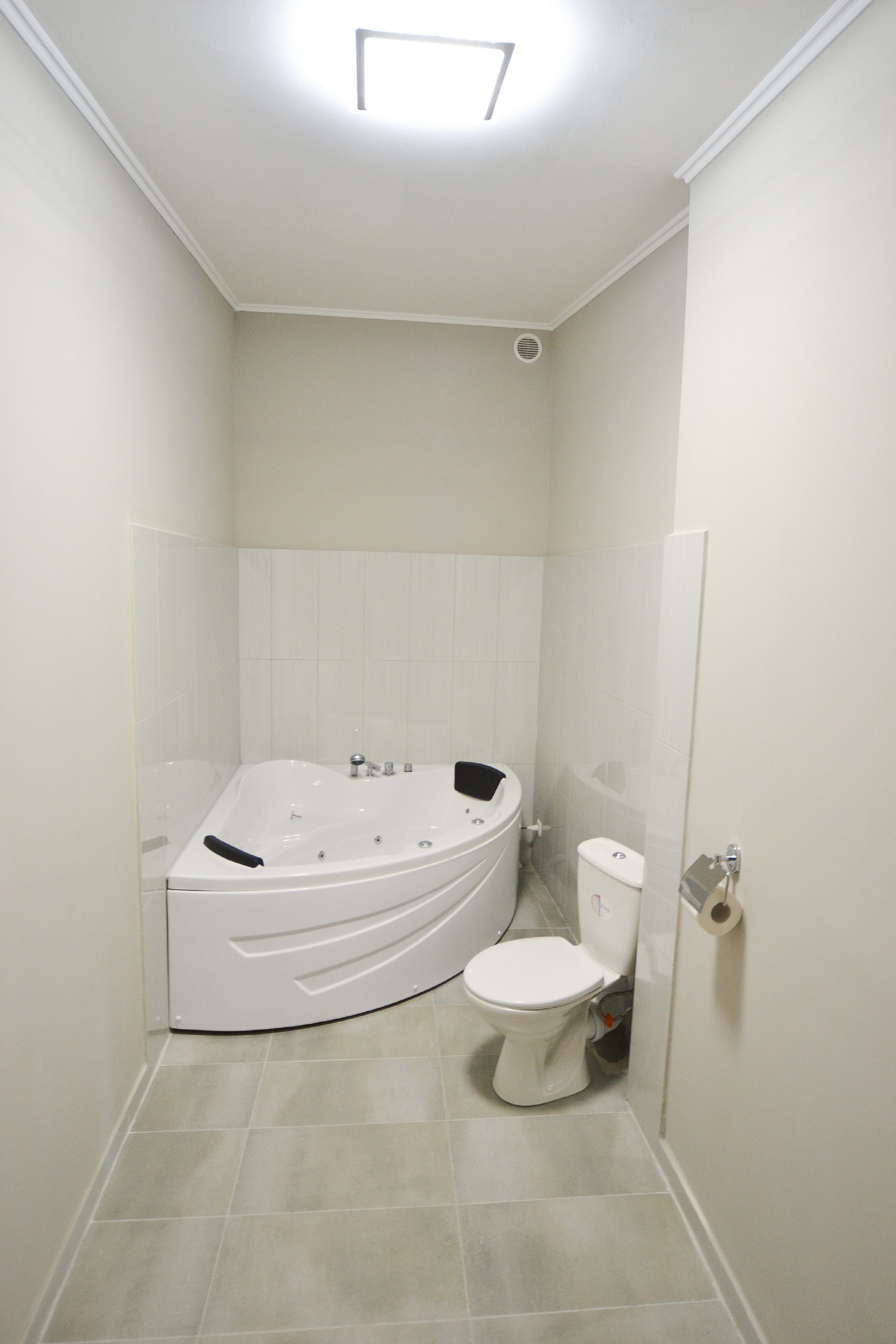 A small, modern bathroom with a white bathtub, toilet, and tiled floor.