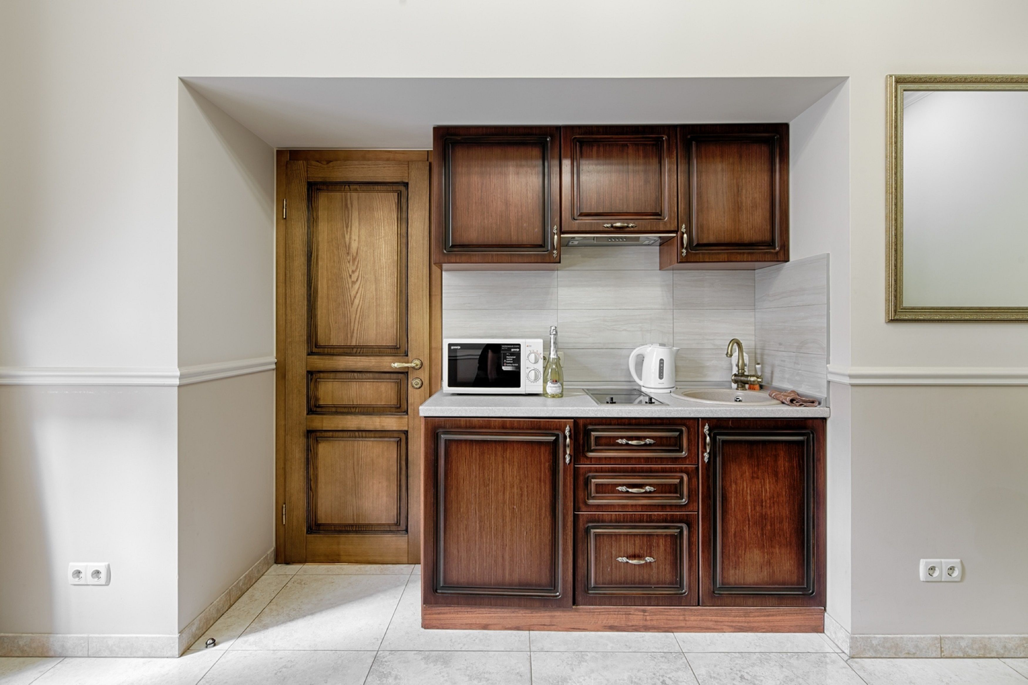 A compact kitchen with wooden cabinets, a microwave, a kettle, and a sink.