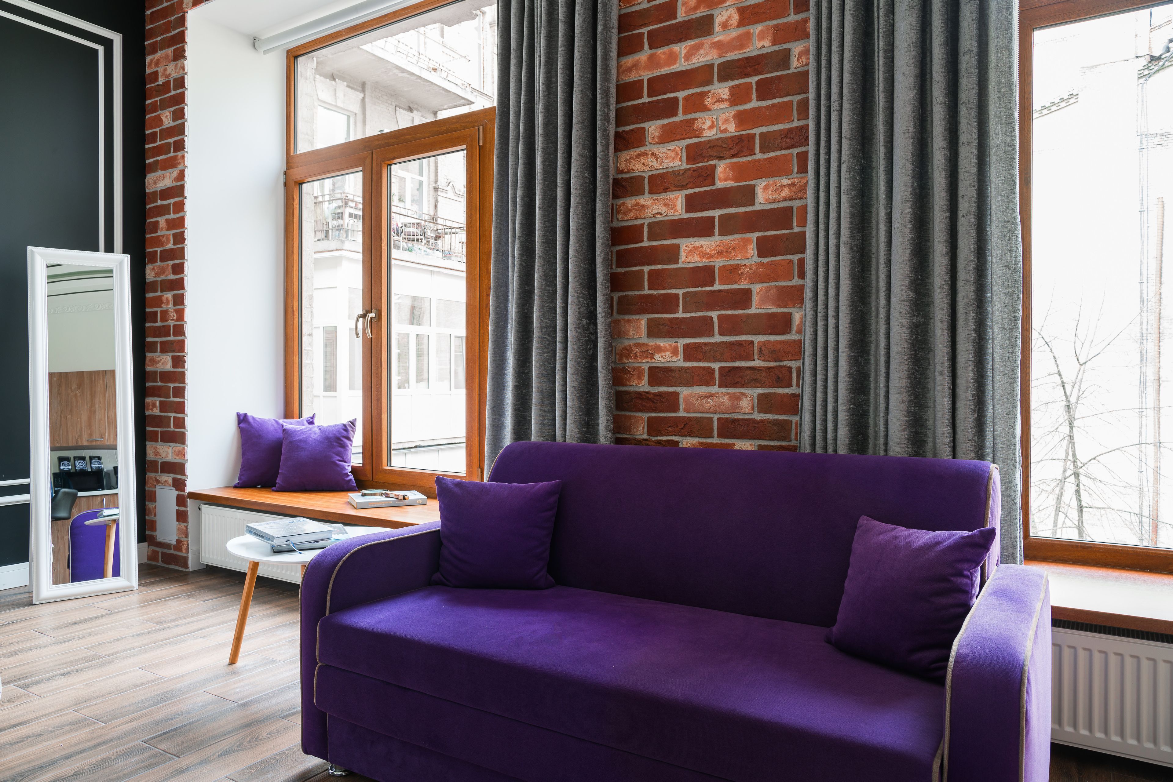 Un salon moderne avec un canapé violet, une table en bois et une vue sur le paysage urbain, visible à travers de grandes fenêtres.