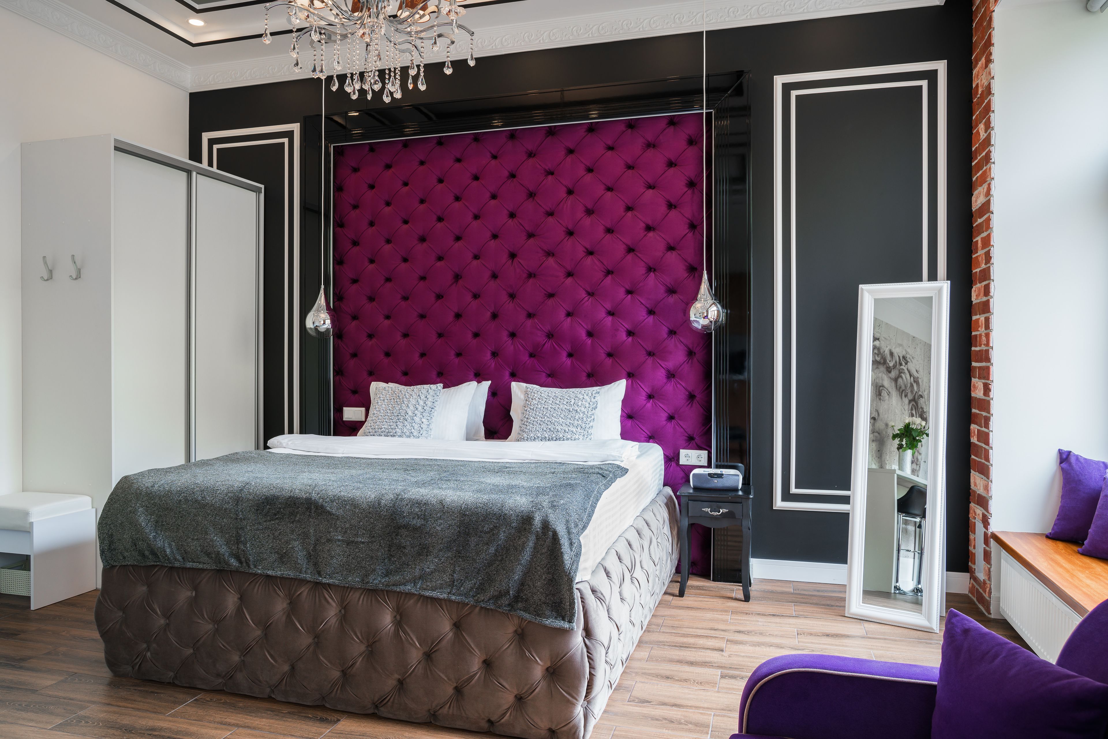 A modern bedroom with a tufted headboard, a large bed, a nightstand, and a mirror.