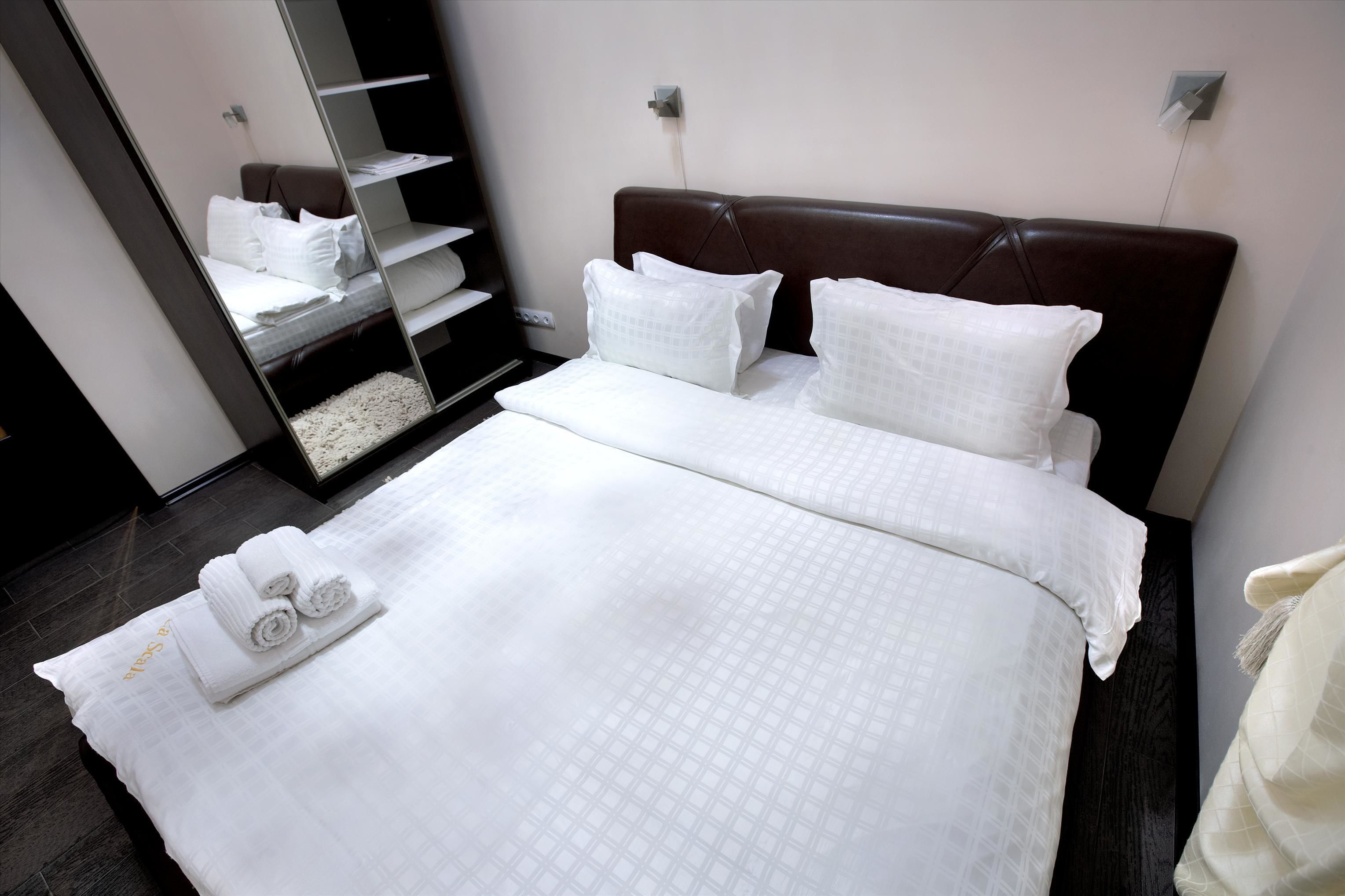 Un lit bien fait, avec du linge de lit blanc et des oreillers, une tête de lit marron foncé et une petite table de chevet sur laquelle est posée une serviette enroulée.