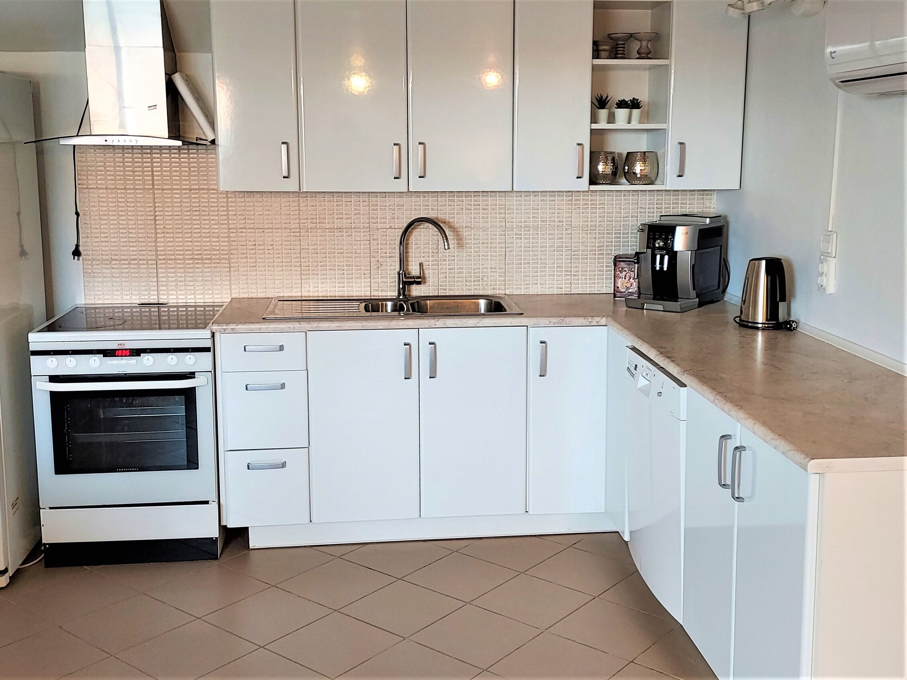 A modern kitchen with white cabinets, a built-in oven, a sink, and a coffee maker.