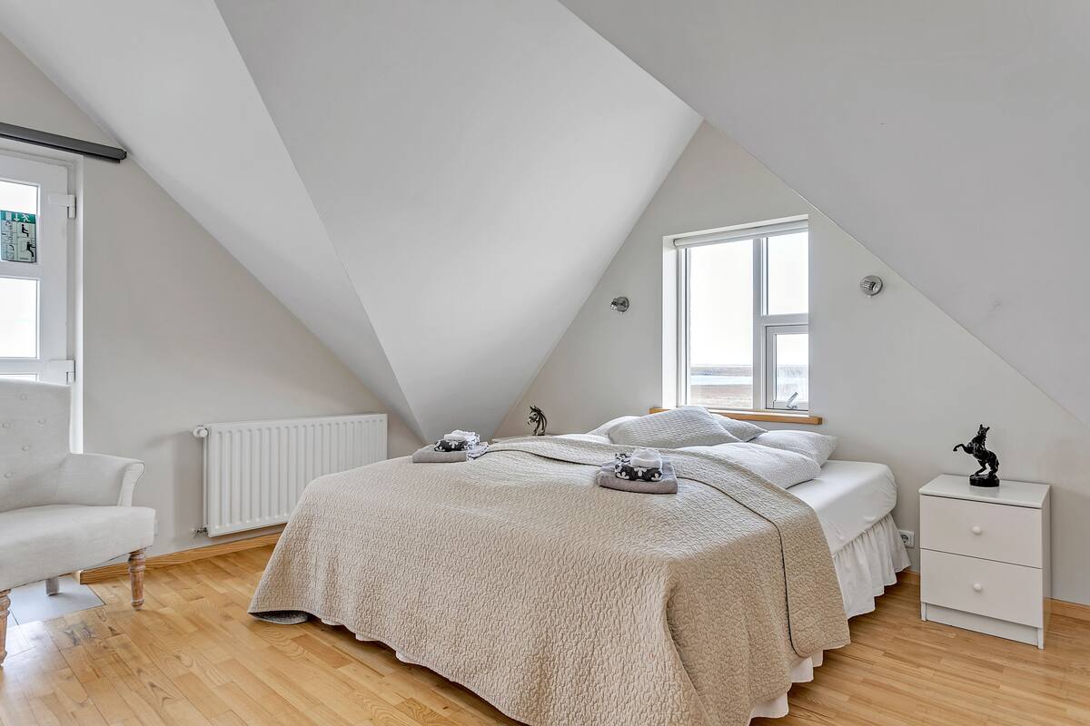 A bedroom with a sloped ceiling, a bed with a white duvet, a nightstand, and a radiator.