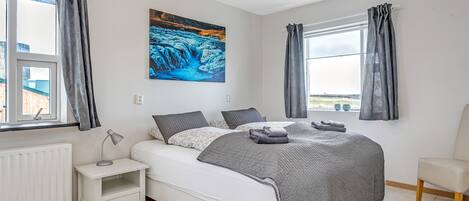 Une chambre à coucher avec un lit, une table de chevet, une chaise, une fenêtre et un tableau au mur.