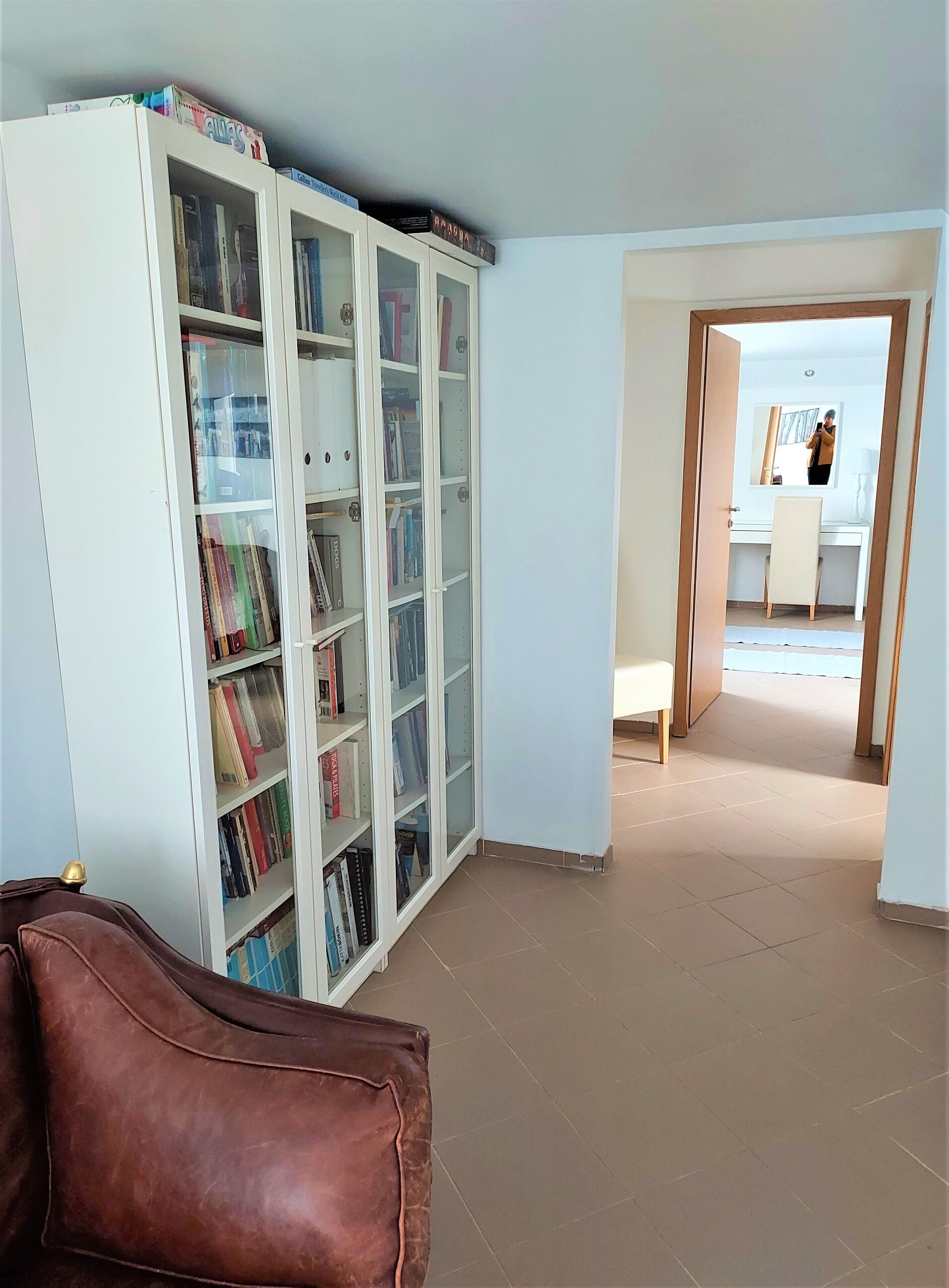 Una habitación con una estantería blanca llena de libros, un sofá de cuero marrón y un escritorio con una silla.