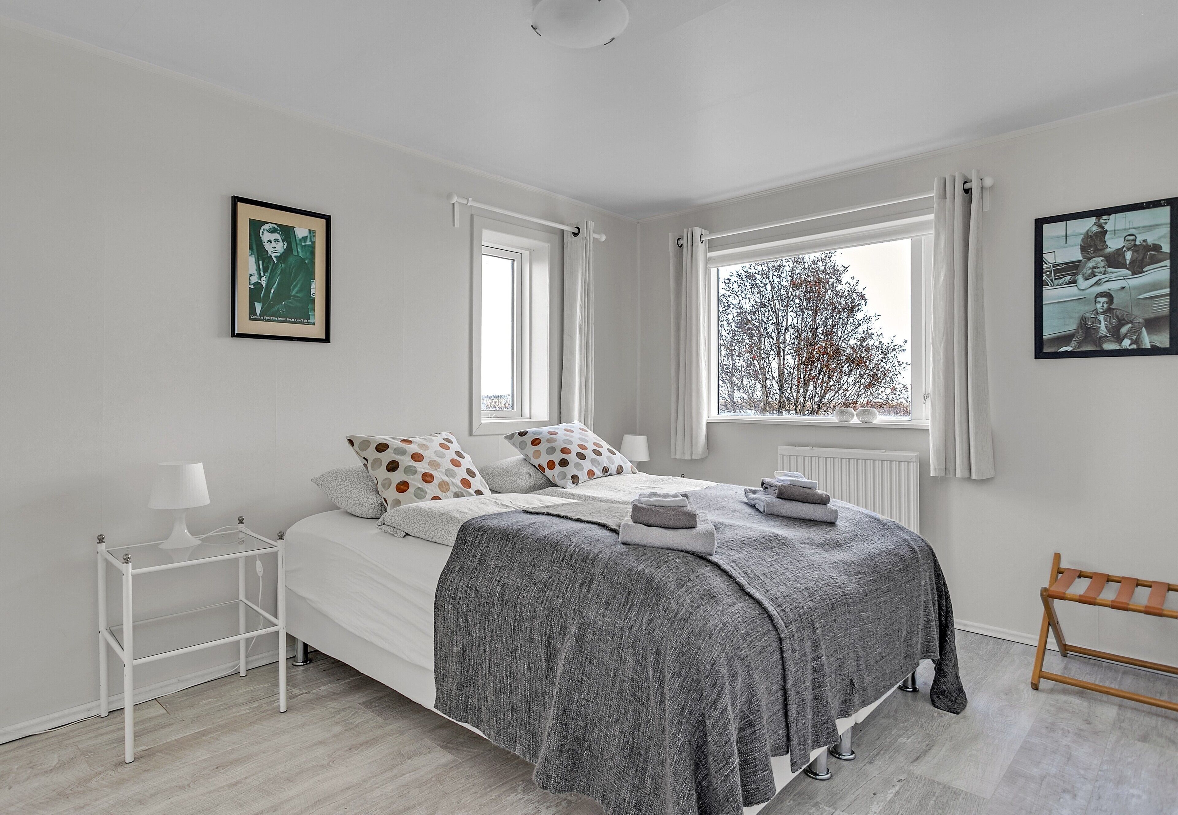 A bedroom with a bed, a side table, a window with curtains, and a picture on the wall.