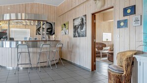 A modern kitchen with a bar area, wooden walls, and a dining area with a unique wooden chair.