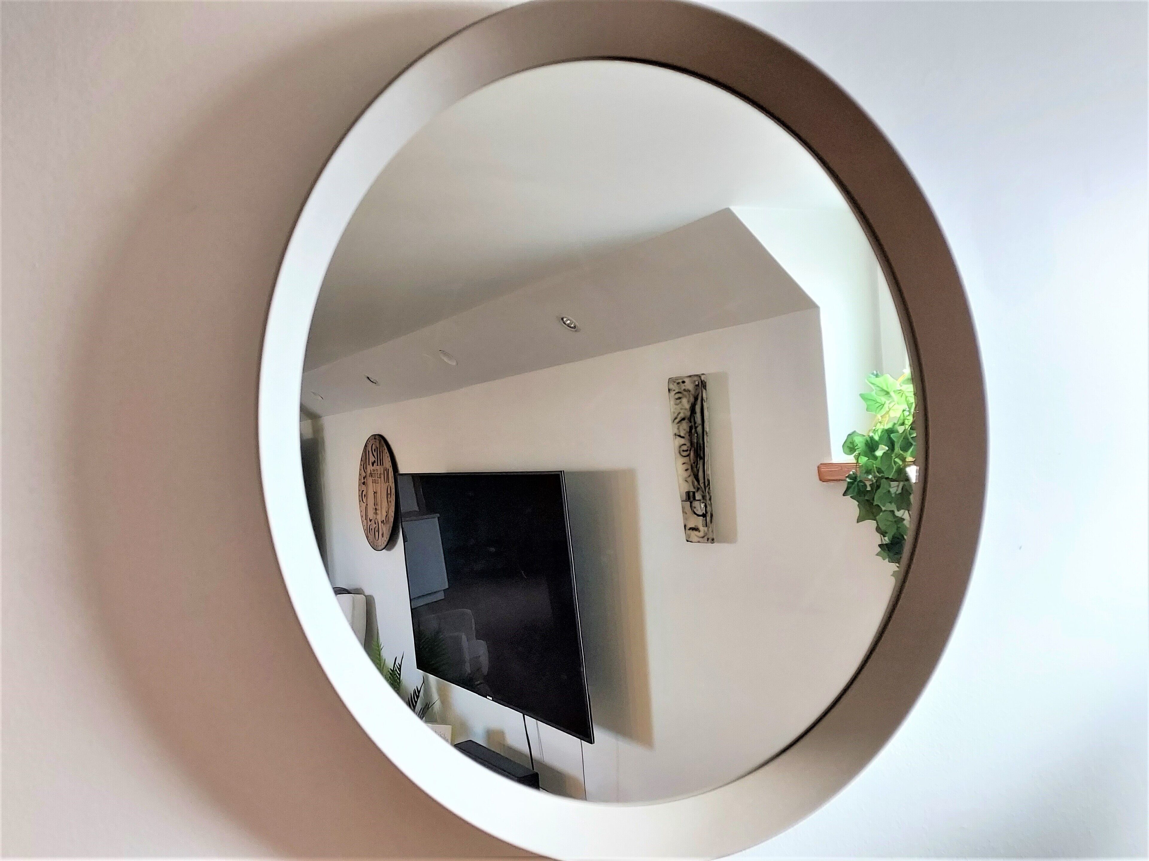 A circular mirror reflecting a room with a flat-screen TV, a plant, and a wall-mounted clock.
