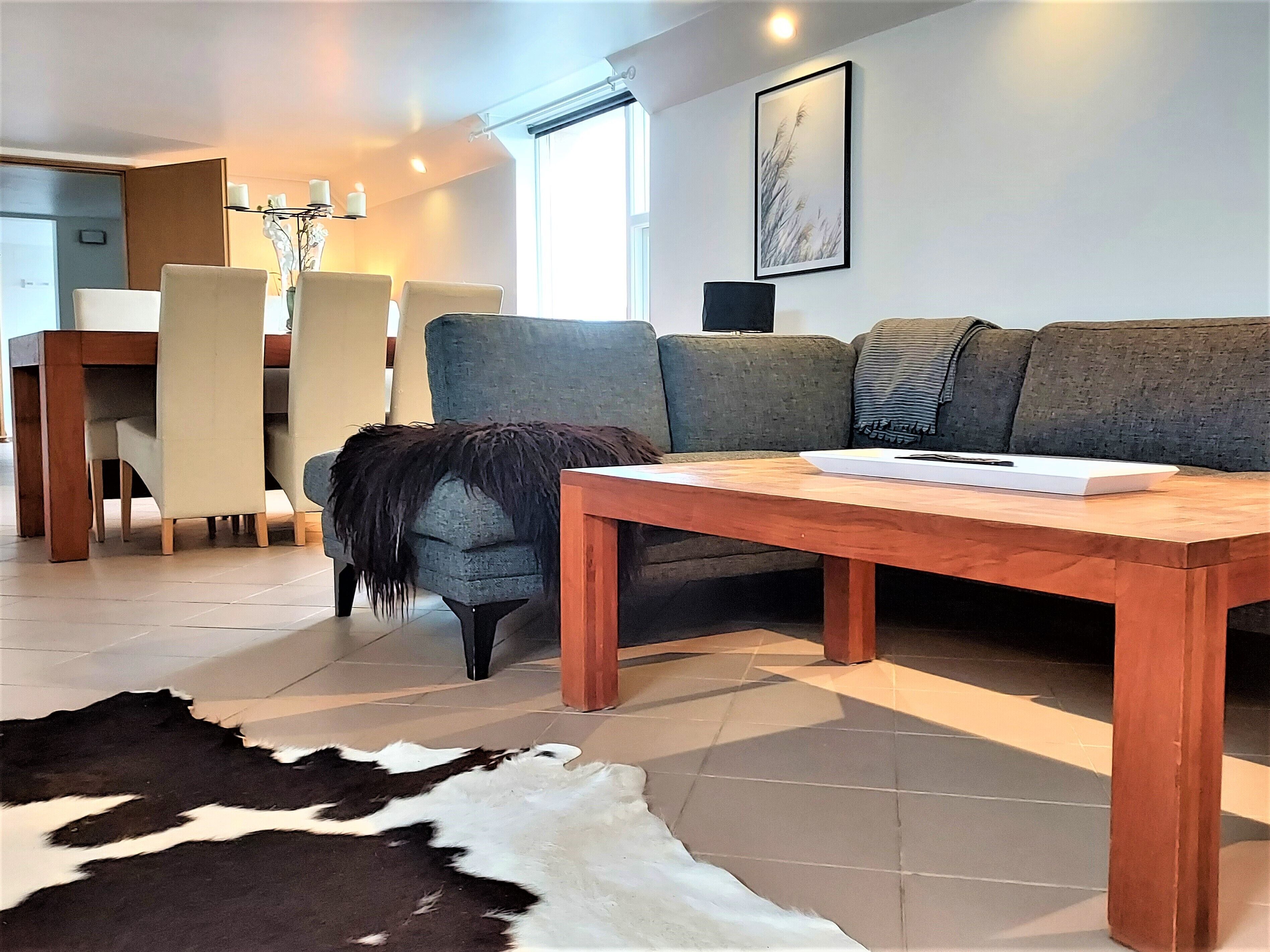 A modern living room with a sofa, a dining table, and a cowhide rug.