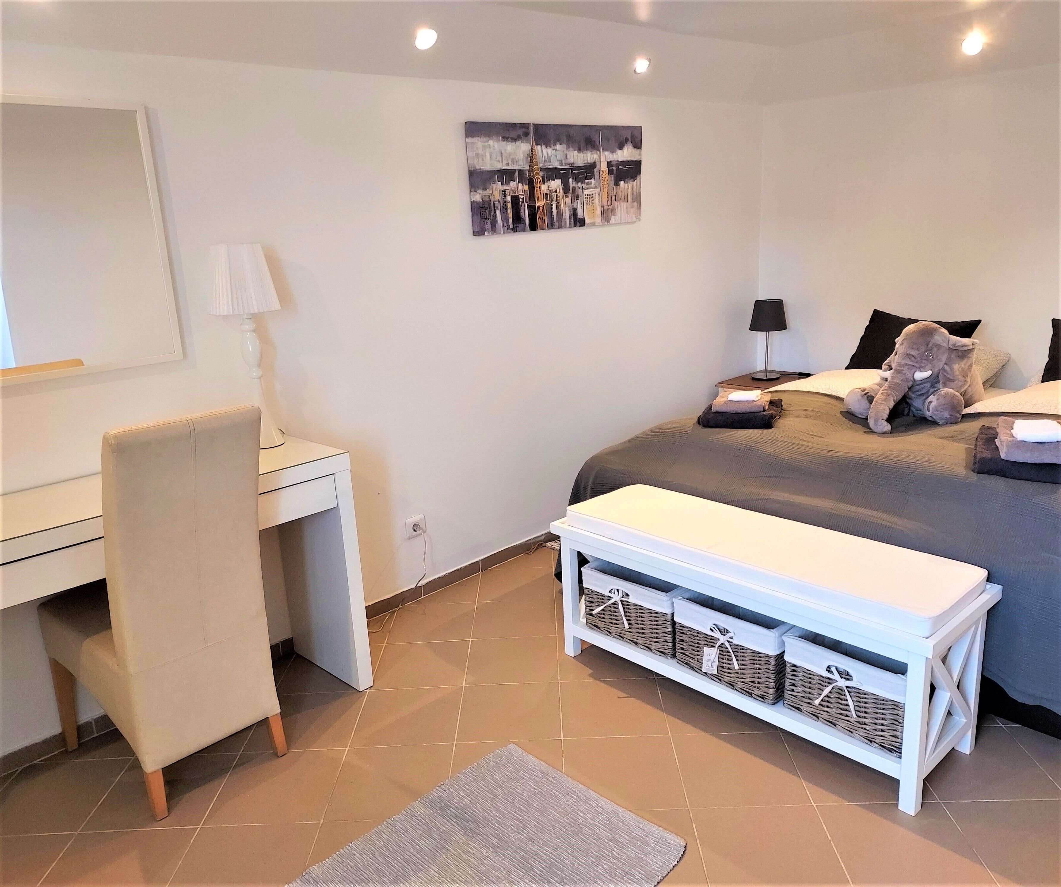 A bedroom with a bed, bedside table, lamp, and a desk with a chair.