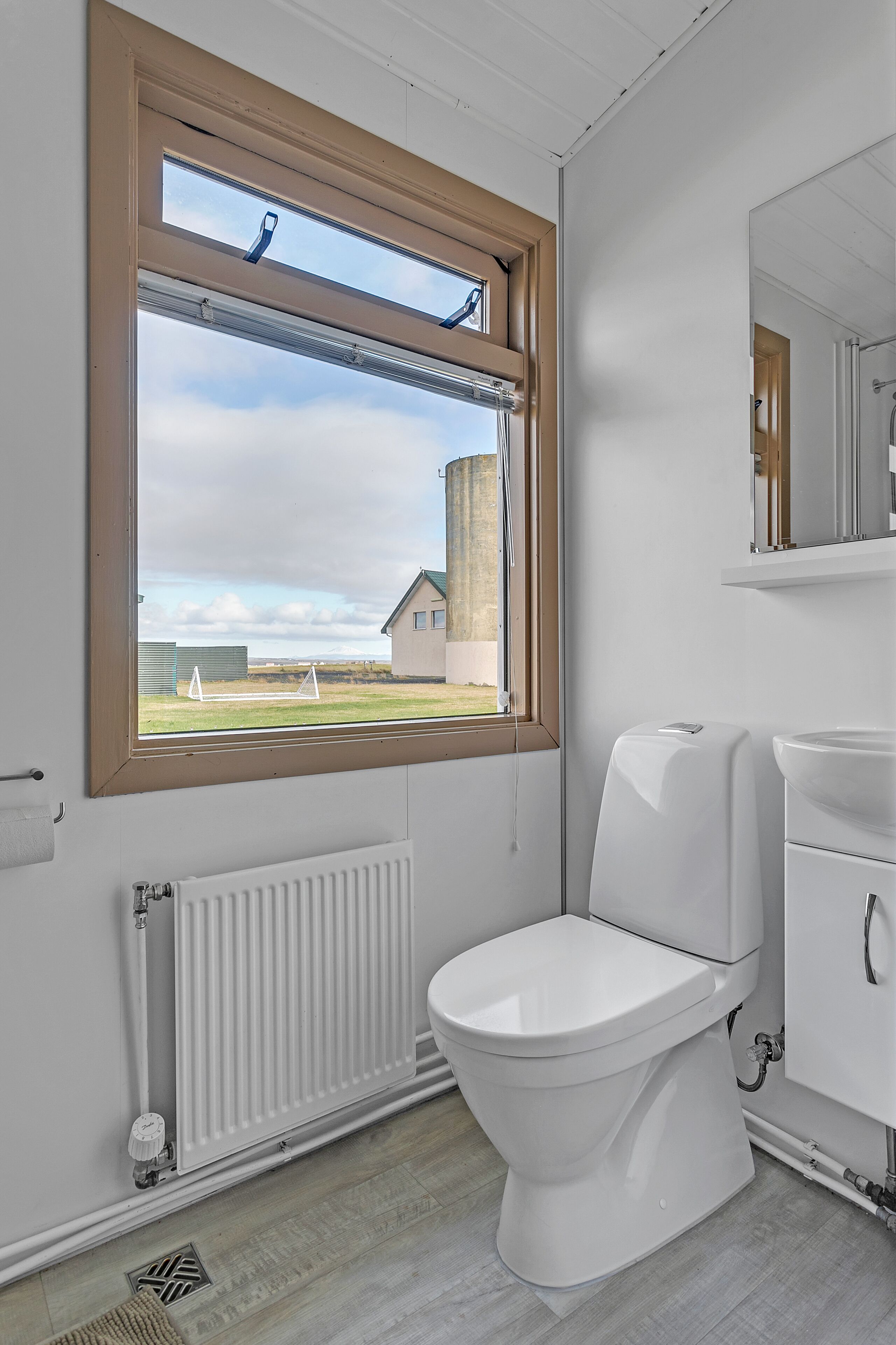 A modern bathroom with a toilet, a sink, and a window with a view of a building and a grassy area.