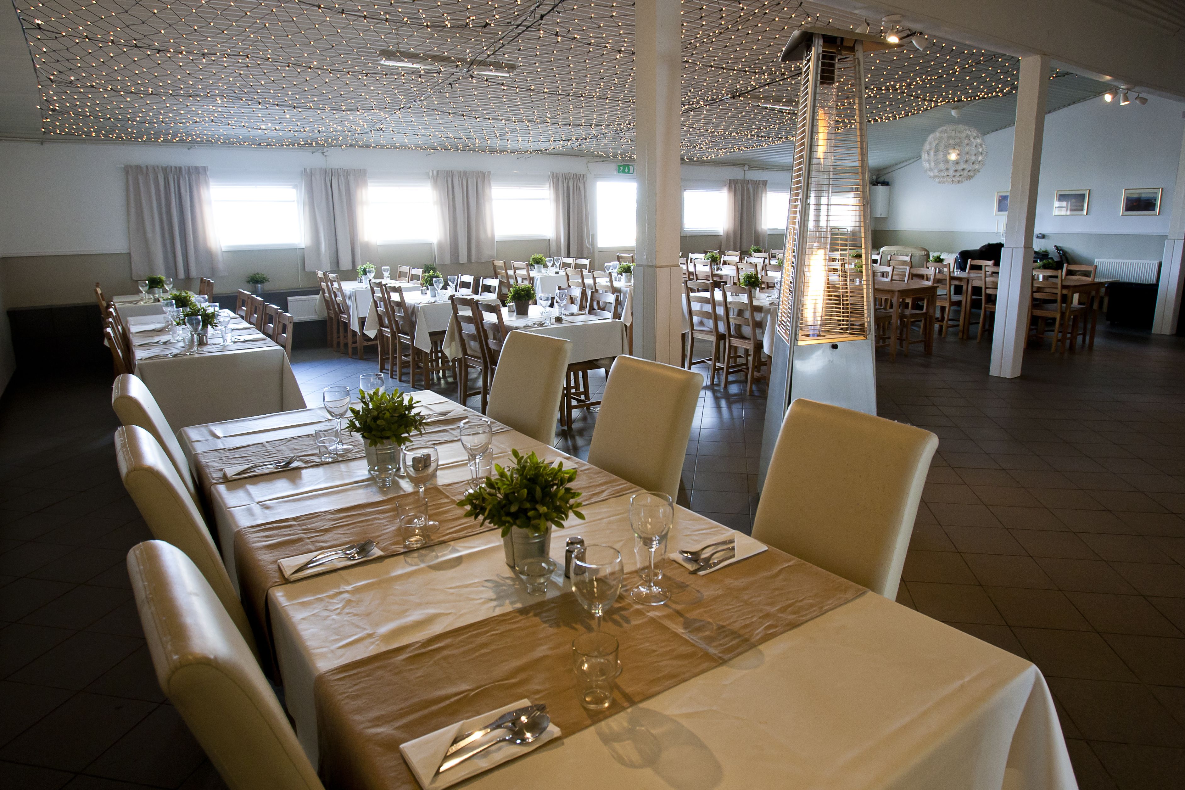A spacious dining area with multiple tables set for guests, featuring a modern ceiling design and natural light from large windows.
