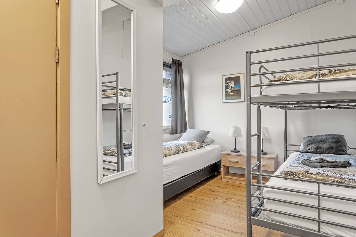 A dormitory room with bunk beds, a bedside table with a lamp, and a window with curtains.