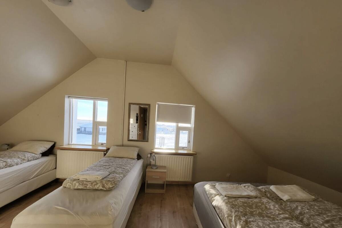 A small, triangular attic bedroom with two beds, a radiator, and a window overlooking a snowy landscape.