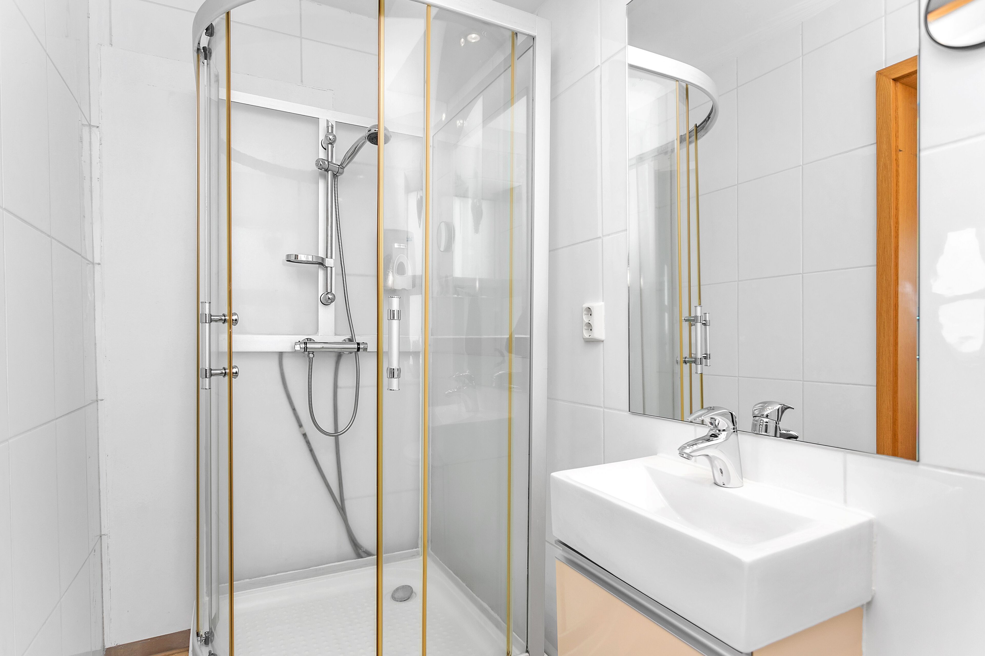 Un baño moderno con ducha acristalada, lavabo blanco y un espejo grande.