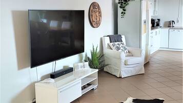 A modern living room with a flat-screen TV, a white sofa, a cowhide rug, and a kitchen in the background.