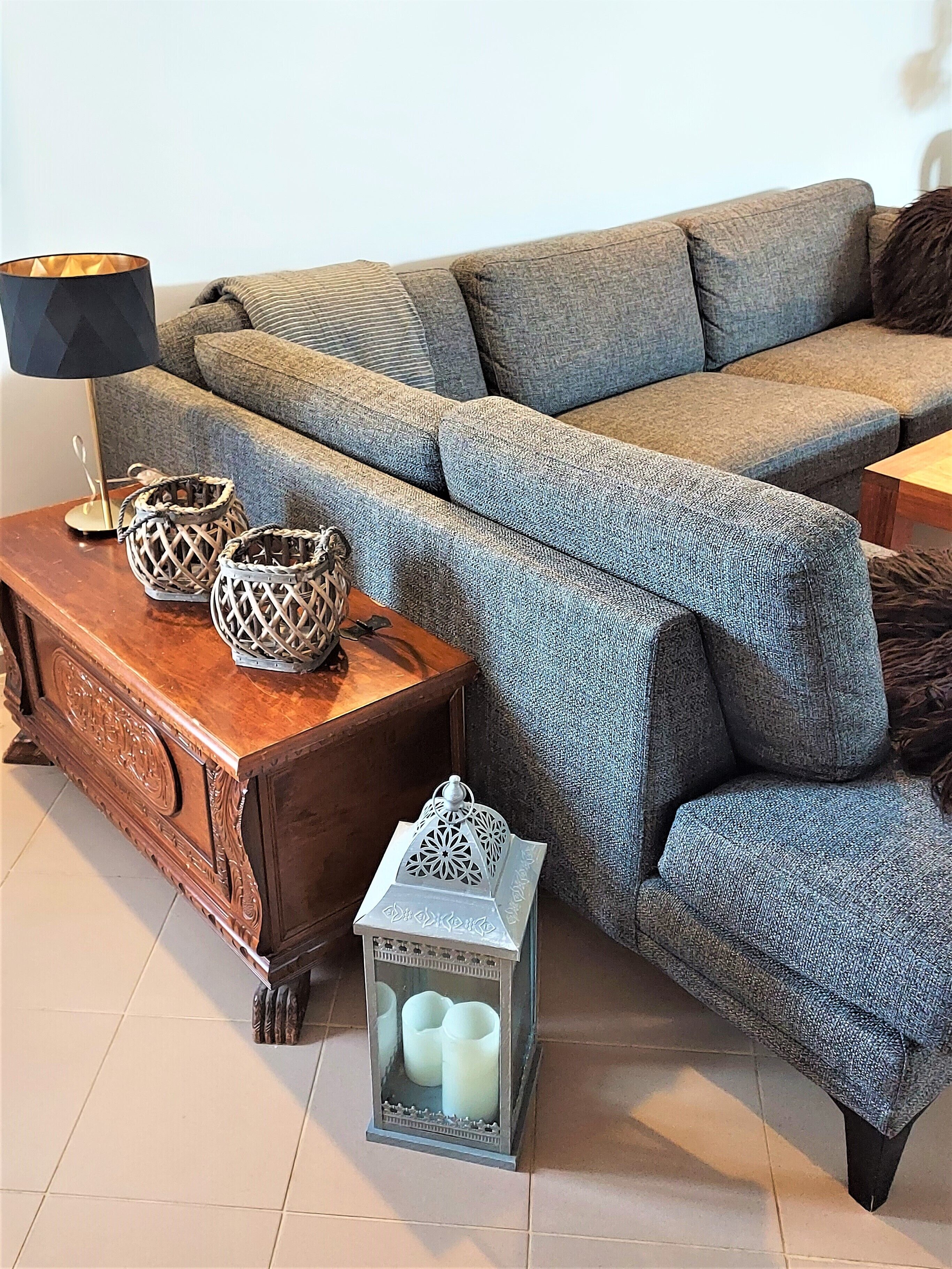 A living room with a grey sofa, a wooden side table, a lamp, and decorative items including a lantern and woven baskets.