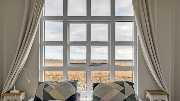 A bedroom with a large window, two bedside tables, and a bed with patterned pillows.