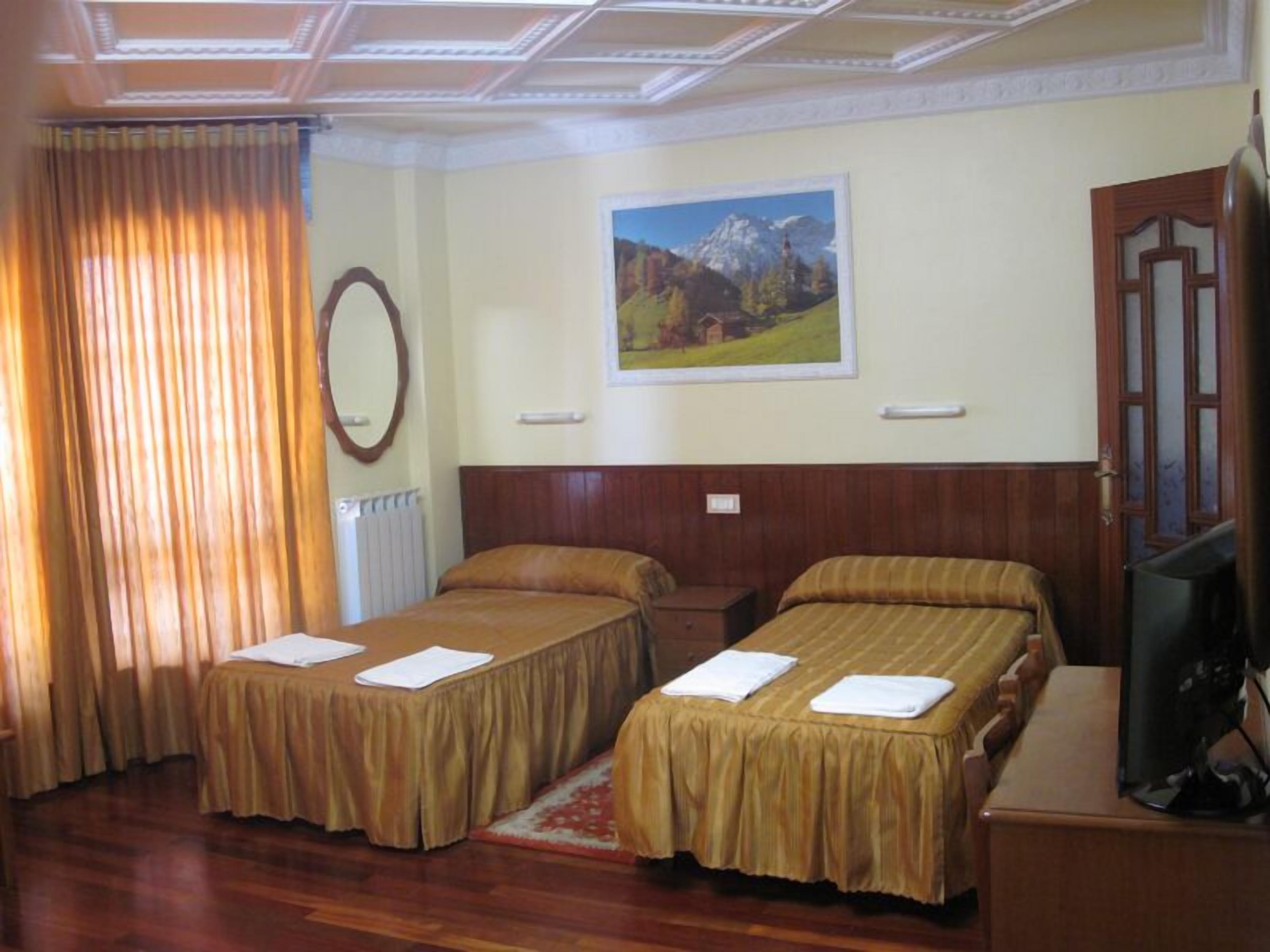Habitación de hotel con dos camas, cabecero de madera, un cuadro de un paisaje montañoso, un espejo y un televisor sobre un mueble de madera.