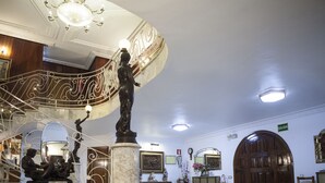 A grand lobby with a marble floor, a statue, a staircase, and a large wooden door.