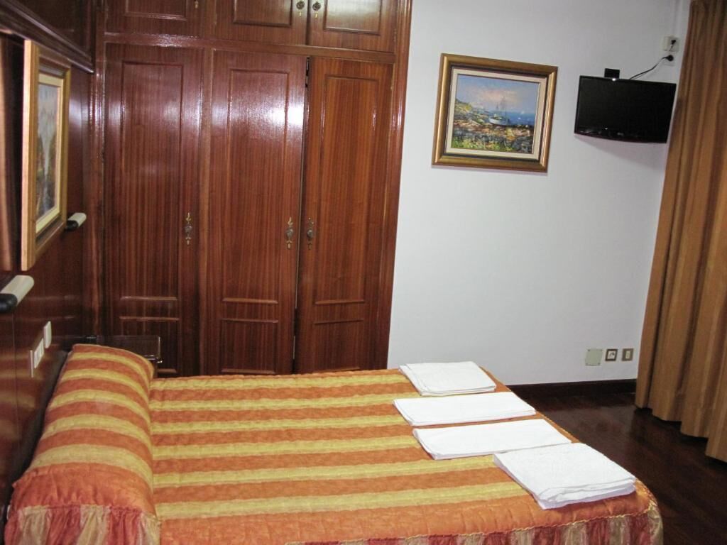 A bedroom with a bed, a wooden wardrobe, a painting on the wall, and a television.